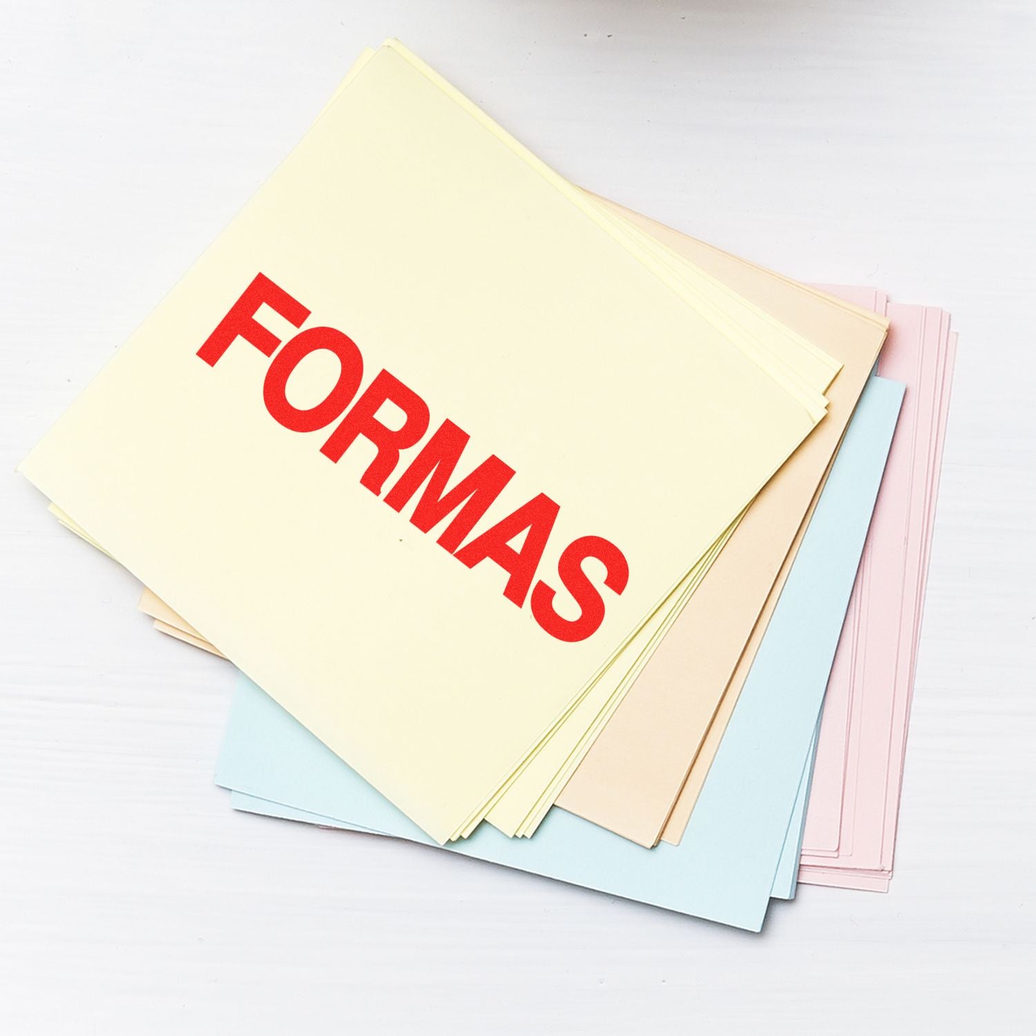 A stack of pastel-colored papers stamped with FORMAS in red using the Formas Rubber Stamp, placed on a white surface.