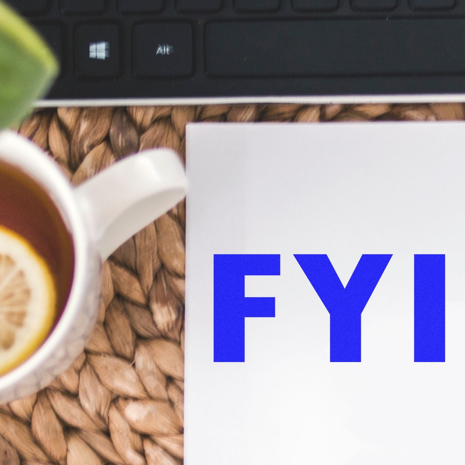 A close-up of a desk with a keyboard, a cup of tea with lemon, and a document stamped with FYI using the FYI Rubber Stamp.