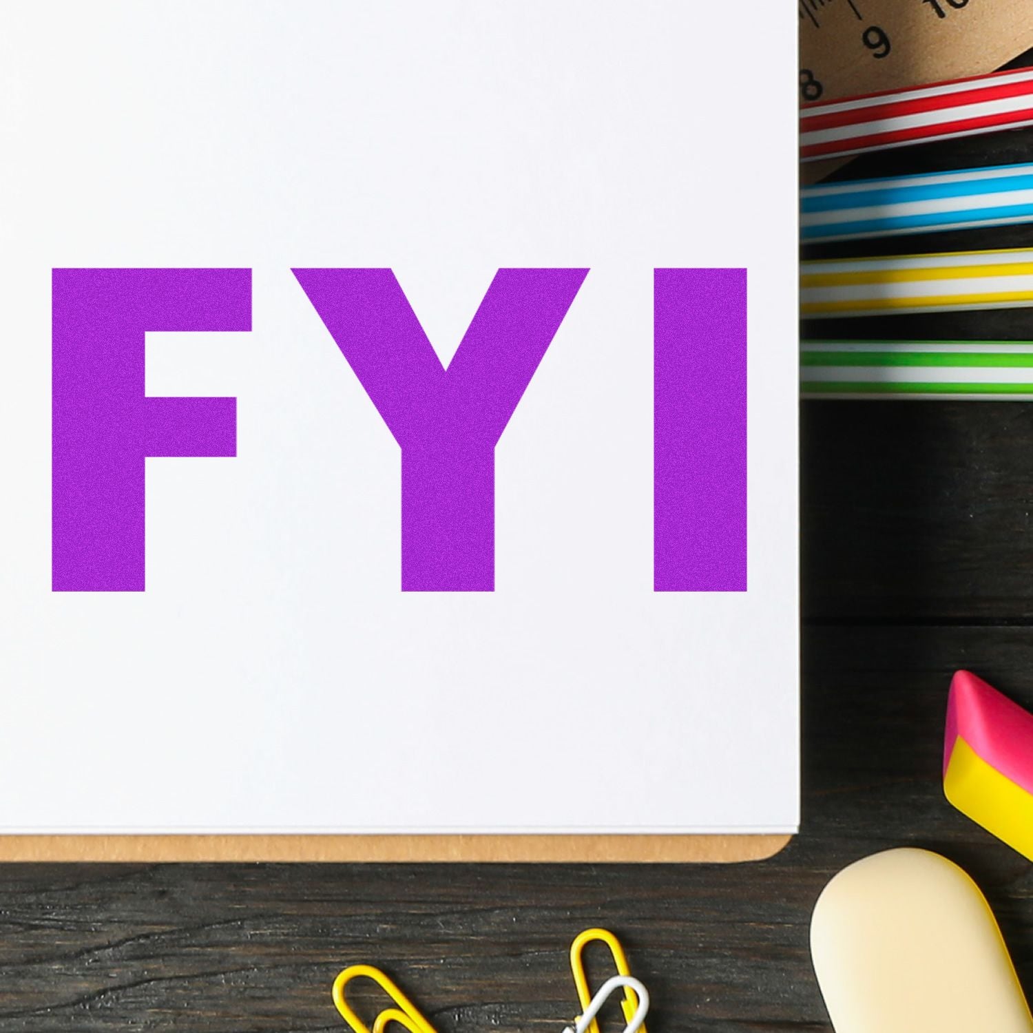 Large Self Inking FYI Stamp in use, displaying bold purple FYI on paper, surrounded by colorful office supplies on a wooden desk.