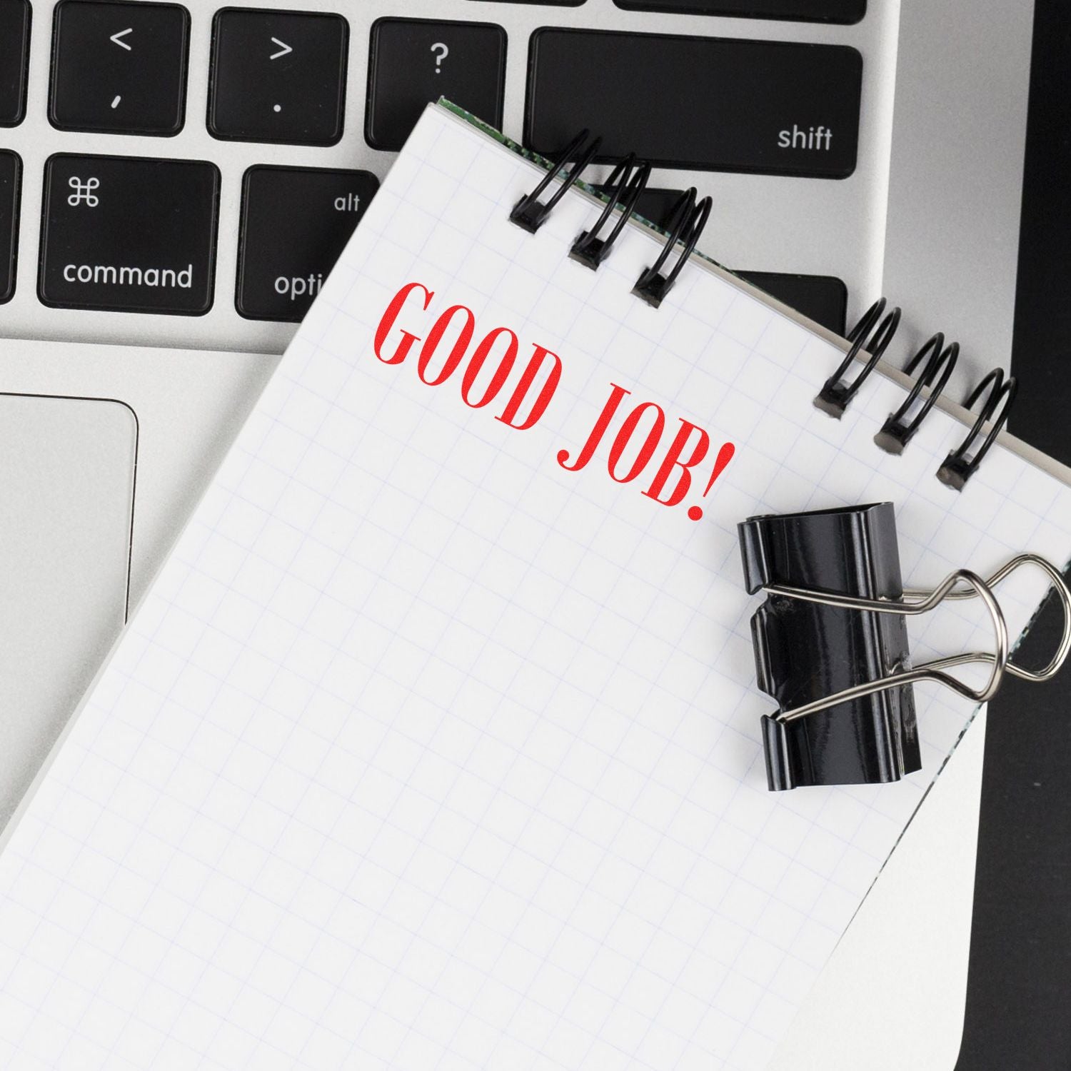 A notepad stamped with GOOD JOB! in red ink using the Good Job Rubber Stamp, placed on a laptop keyboard with a black binder clip.