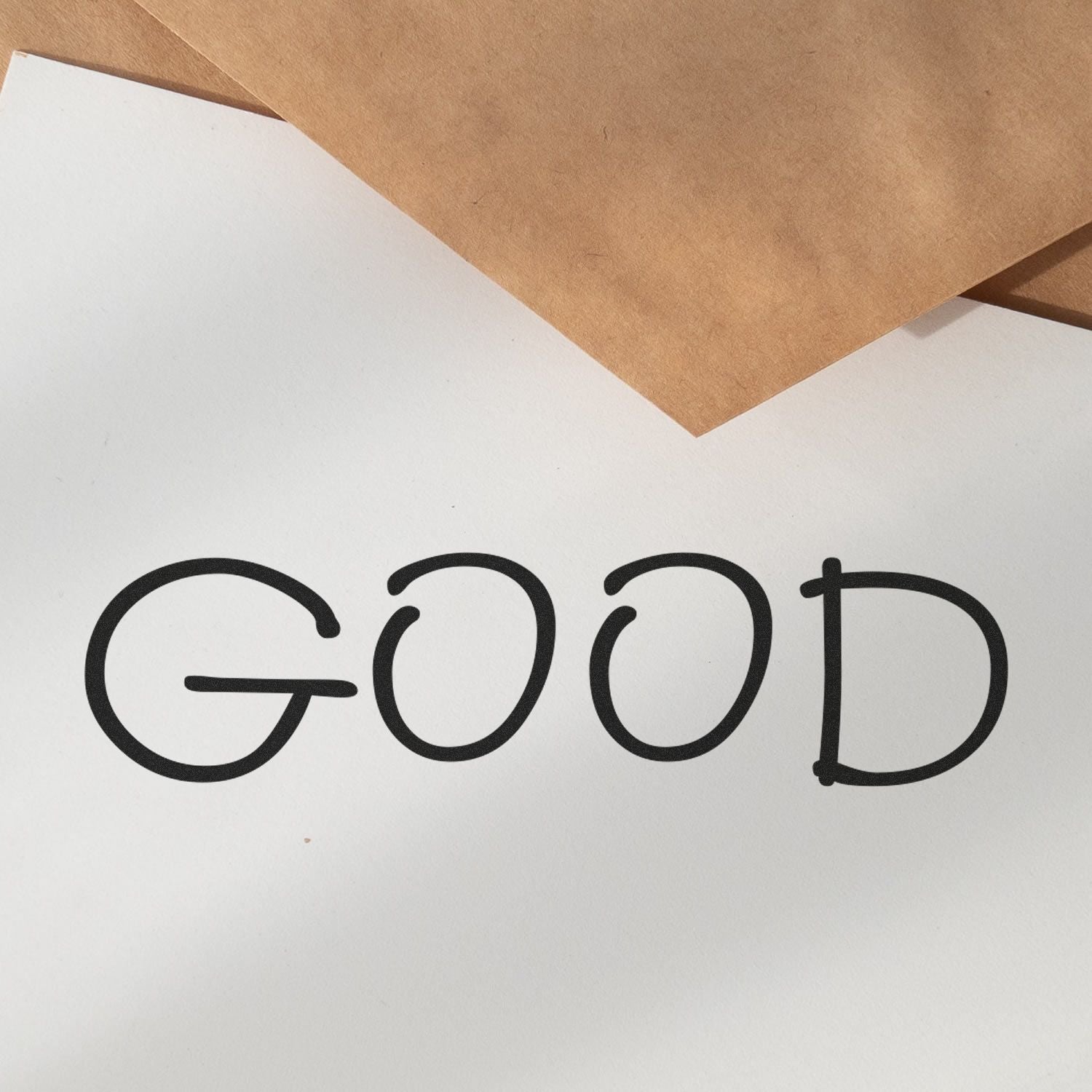 The Good Rubber Stamp imprinting the word GOOD on white paper, with brown envelopes in the background.