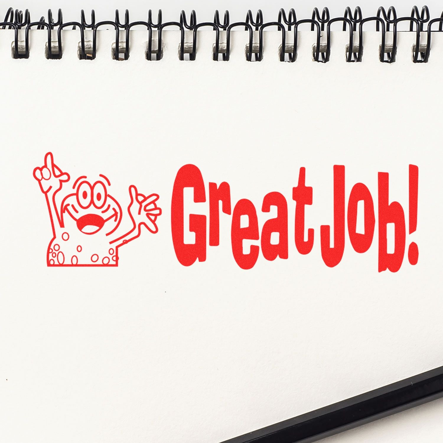 Great Job Rubber Stamp in red ink on a white spiral notebook, featuring a cartoon character with raised hands next to the text.