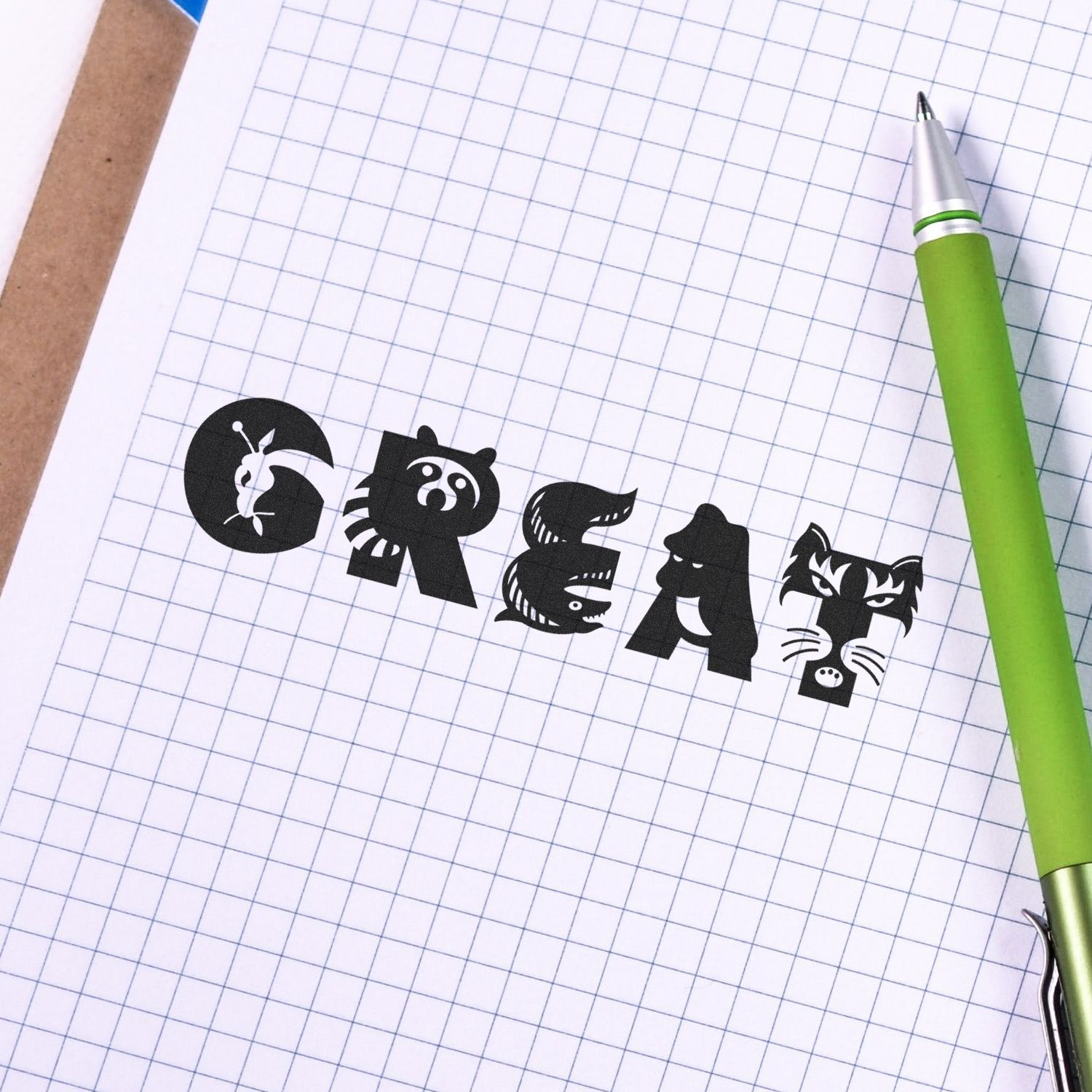 Large Self Inking Great Stamp used on graph paper, spelling out 'GREAT' with animal-themed letters, next to a green pen.