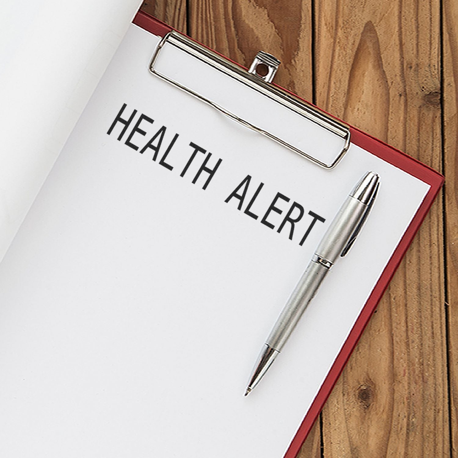 Clipboard with paper stamped Health Alert using the Large Self Inking Health Alert Stamp, with a pen placed beside it on a wooden surface.