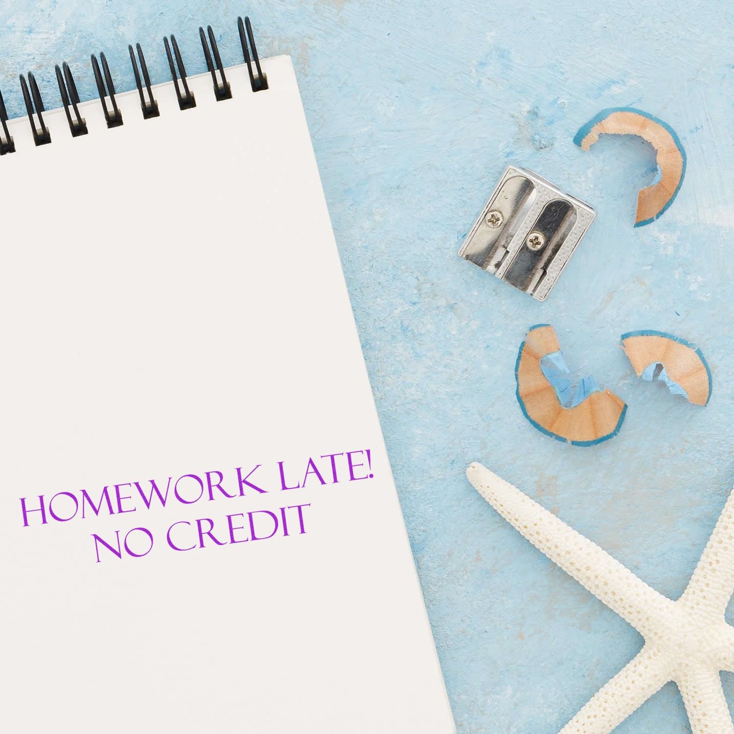 Large Homework Late No Credit Rubber Stamp used on a notebook page, with a pencil sharpener, shavings, and a starfish on a blue background.