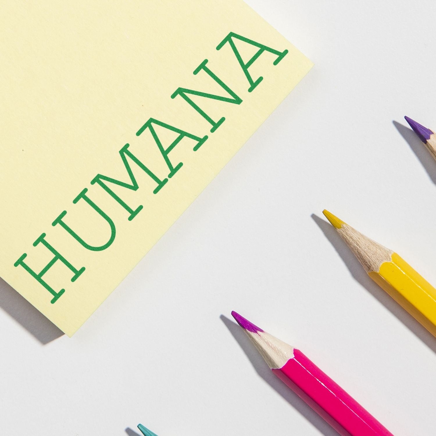 Humana Rubber Stamp imprint on yellow paper with colorful pencils nearby on a white surface.