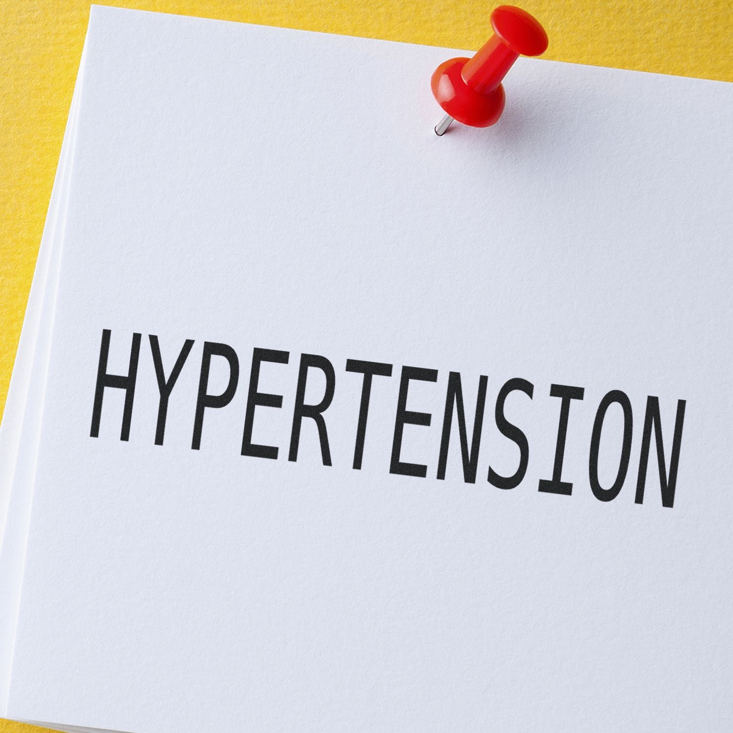 A white paper stamped with HYPERTENSION using the Hypertension Rubber Stamp, pinned to a yellow background with a red pushpin.