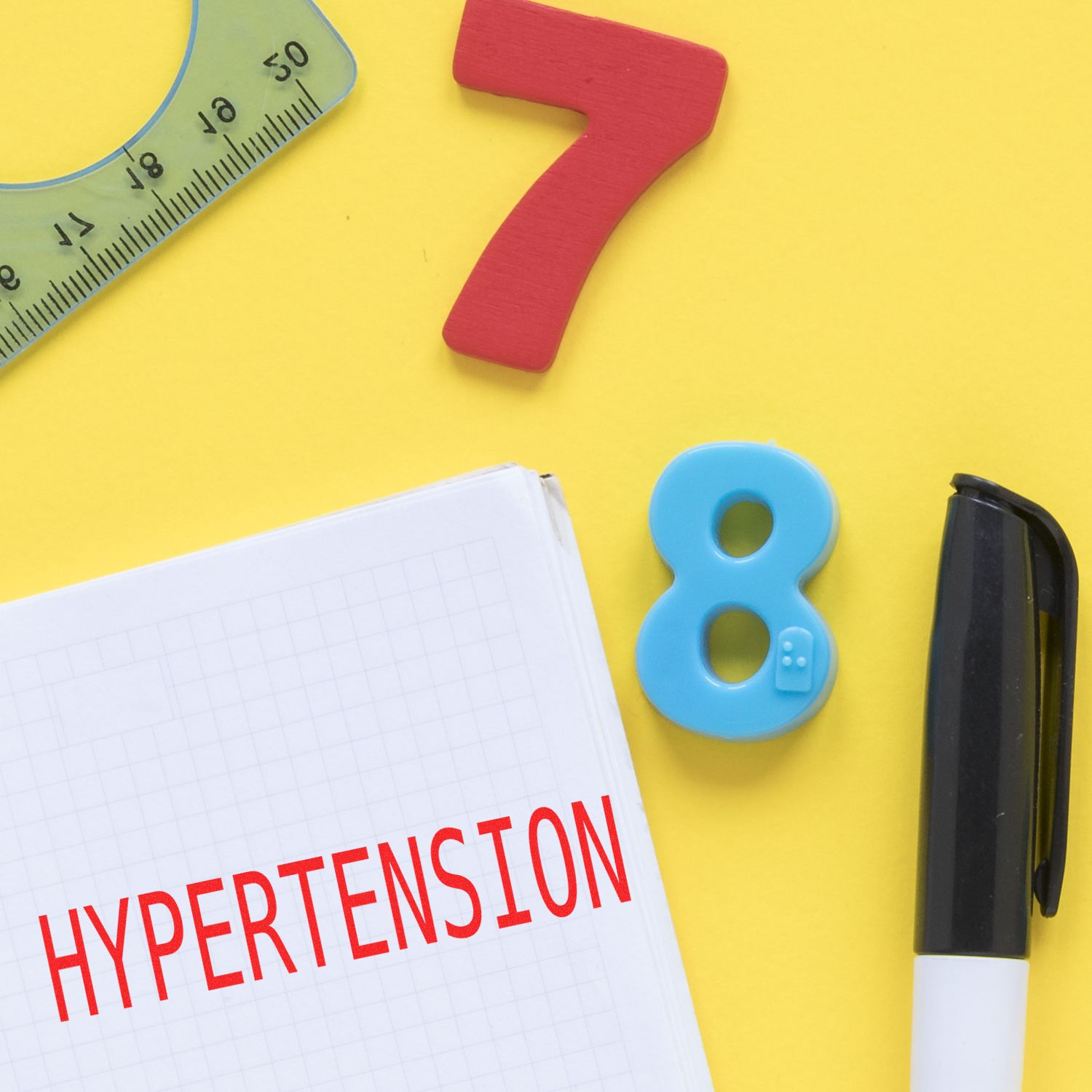 Slim Pre-Inked Hypertension Stamp used on a notebook with a pen, ruler, and colorful numbers on a yellow background.