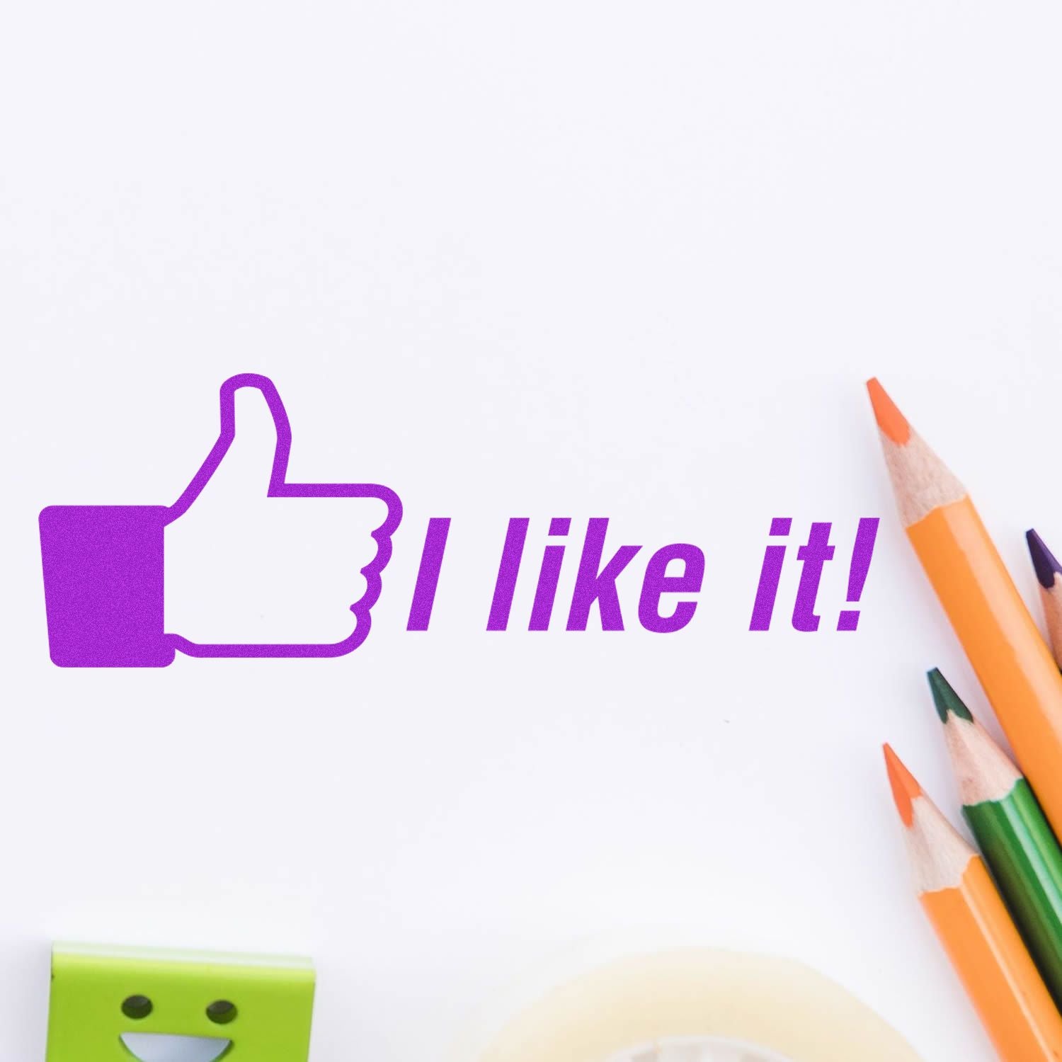 Slim Pre-Inked I like it Stamp in purple ink with a thumbs-up symbol, next to colorful pencils and a green eraser.