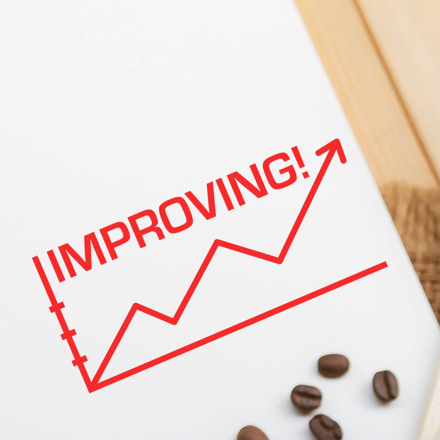 Improving with Chart Icon Rubber Stamp in red ink on white paper, showing an upward trend graph. Coffee beans and wooden surface in the background.