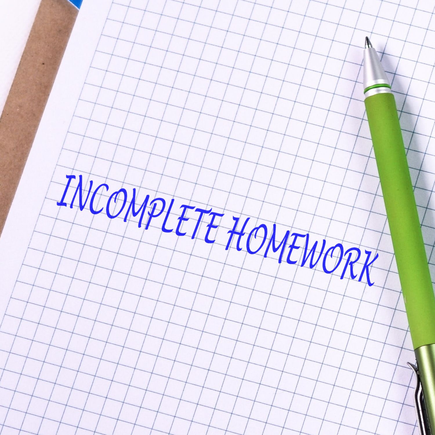 A green pen rests on graph paper stamped with INCOMPLETE HOMEWORK in blue ink using the Incomplete Homework Rubber Stamp.