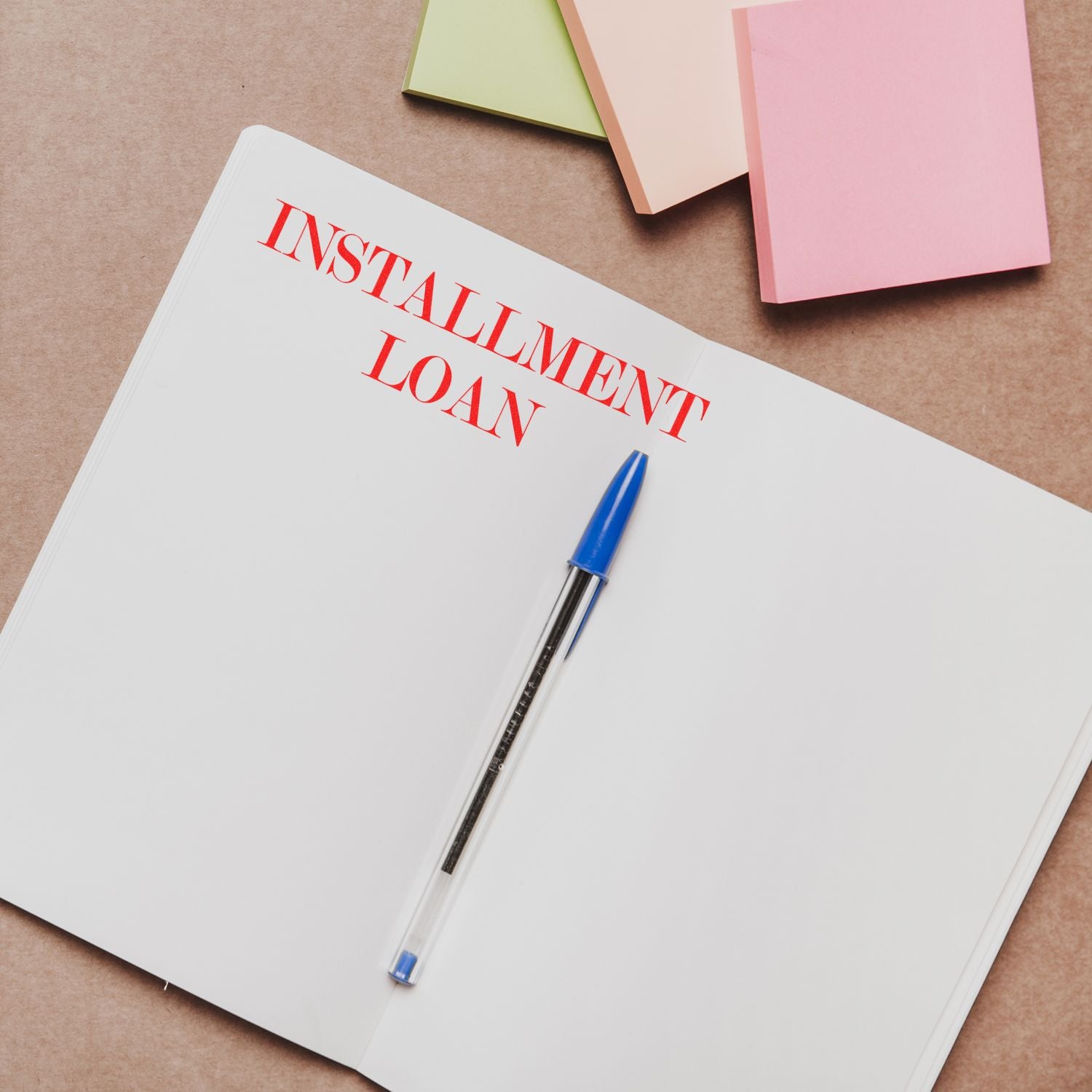 A Self Inking Installment Loan Stamp marks INSTALLMENT LOAN in red on an open notebook, with a blue pen and colorful sticky notes nearby.