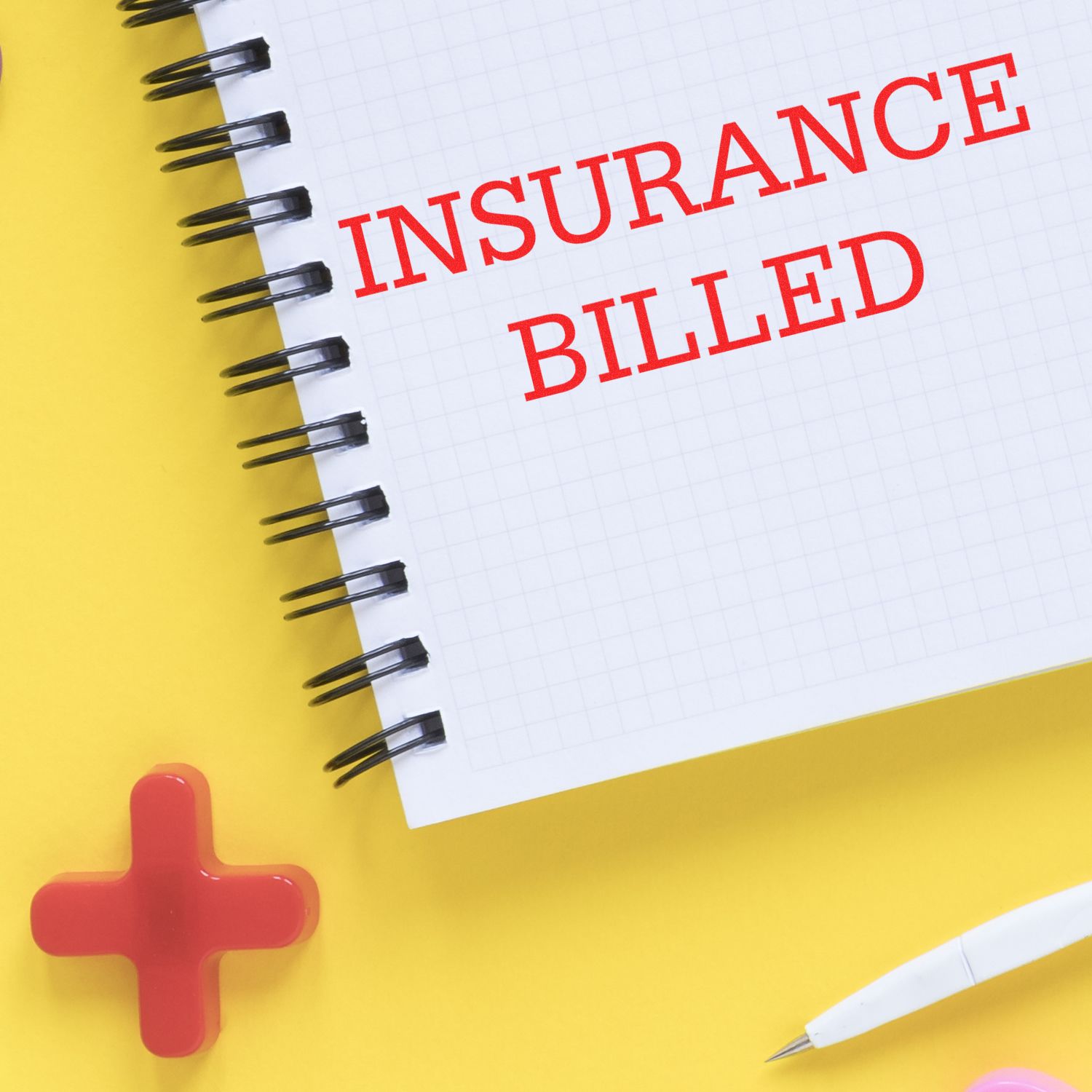 Self Inking Insurance Billed Stamp marking INSURANCE BILLED in red on a spiral notebook, with a red cross and pen nearby on a yellow background.