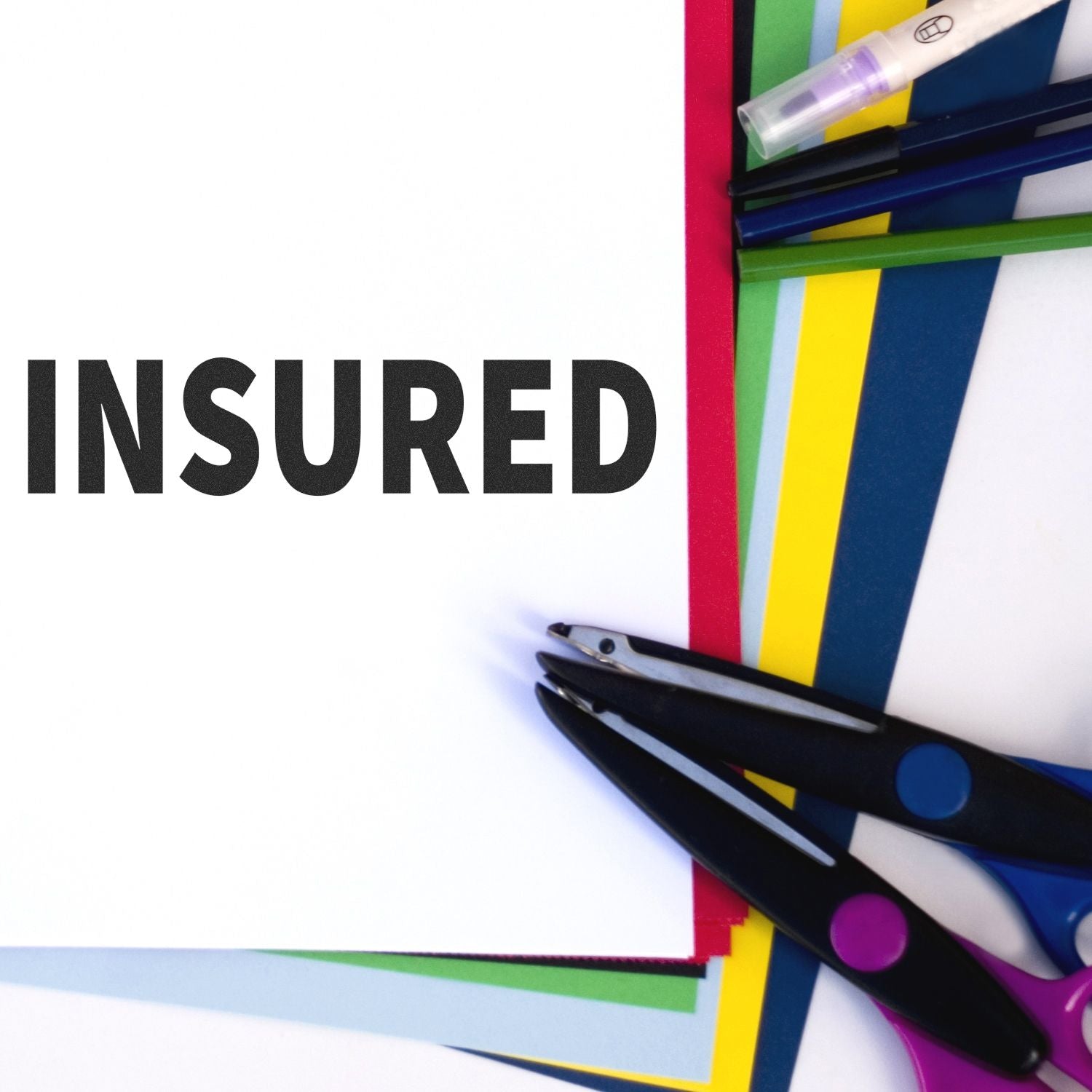 Large Insured Rubber Stamp used on white paper, surrounded by colorful sheets, scissors, and pens.