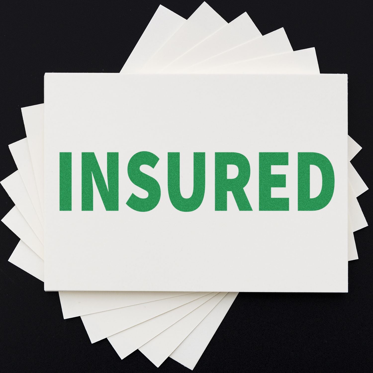 A stack of white cards stamped with INSURED in green using a Slim Pre-Inked Insured Stamp, displayed on a black background.