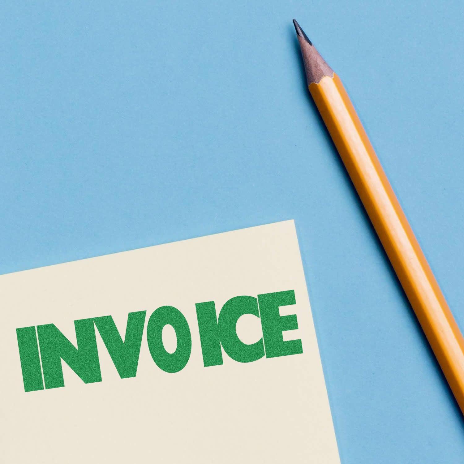 Large Self Inking Invoice Stamp in green ink on a paper next to a sharpened yellow pencil on a blue background.