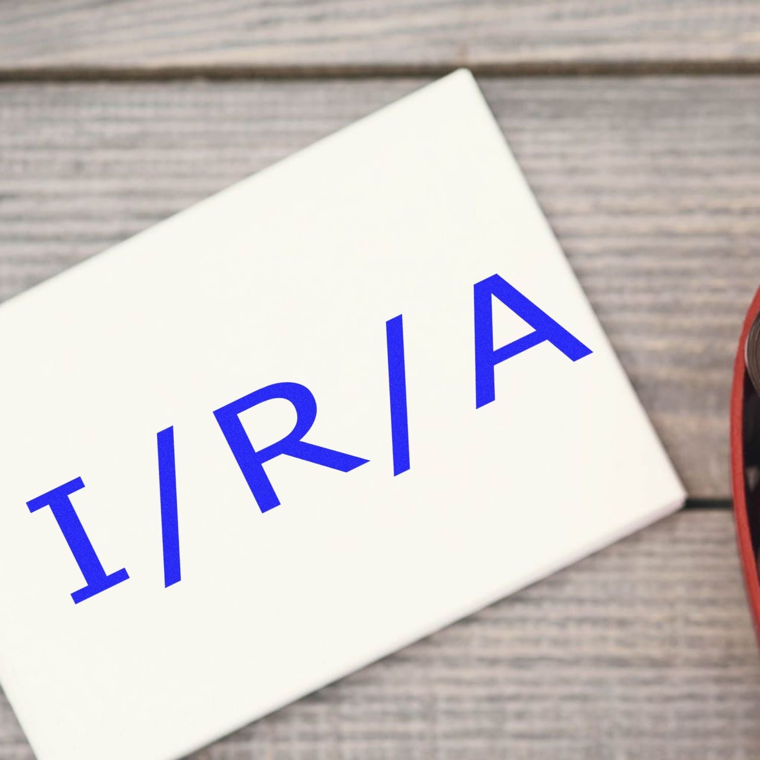 Self Inking Ira Stamp in use on a white envelope, showing clear blue IRA text on a wooden surface background.