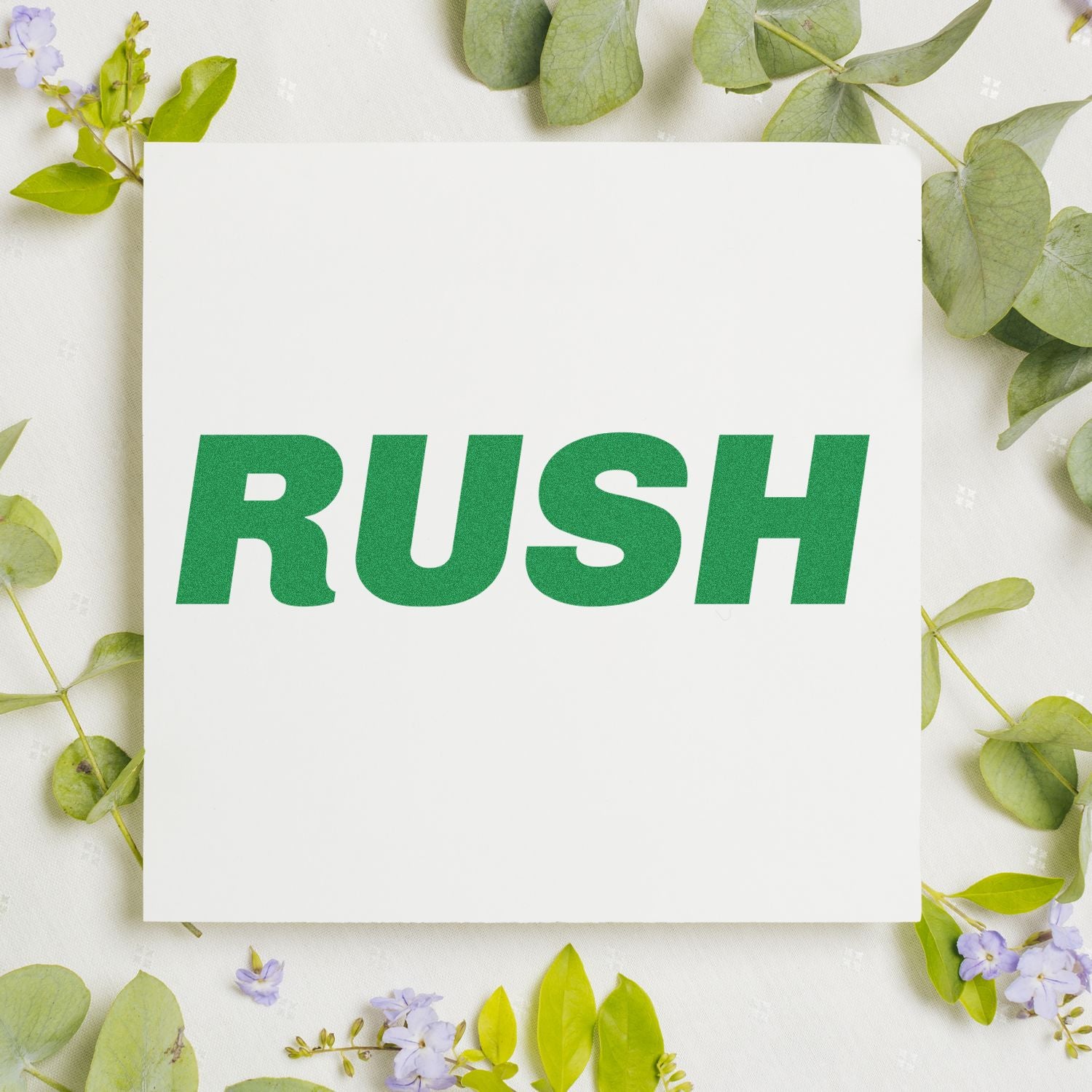 Green 'RUSH' text stamped on white paper using the Italic Rush Rubber Stamp, surrounded by green leaves and small purple flowers.