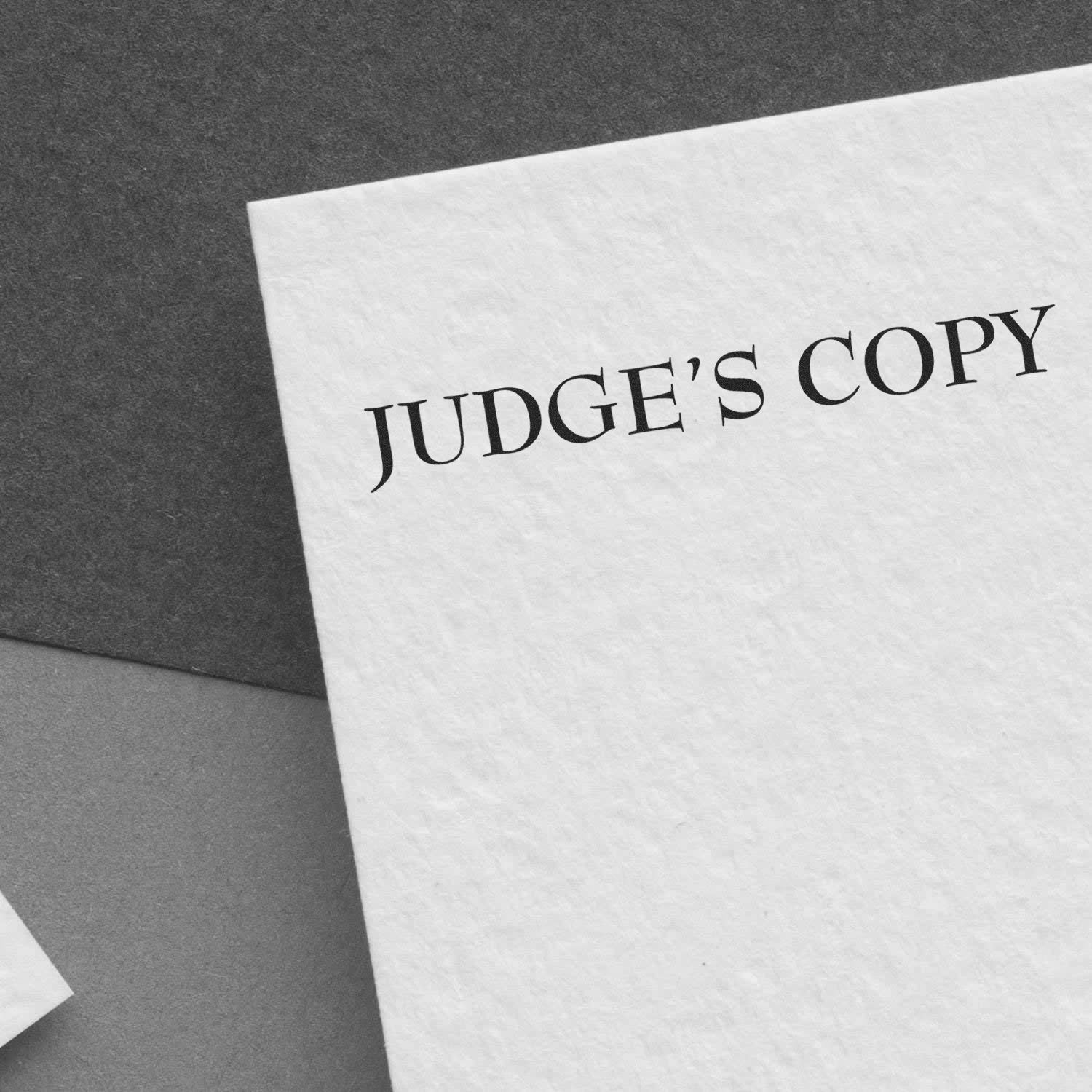 Slim Pre-Inked Judges Copy Stamp marking JUDGE'S COPY on a white paper, placed on a dark surface.