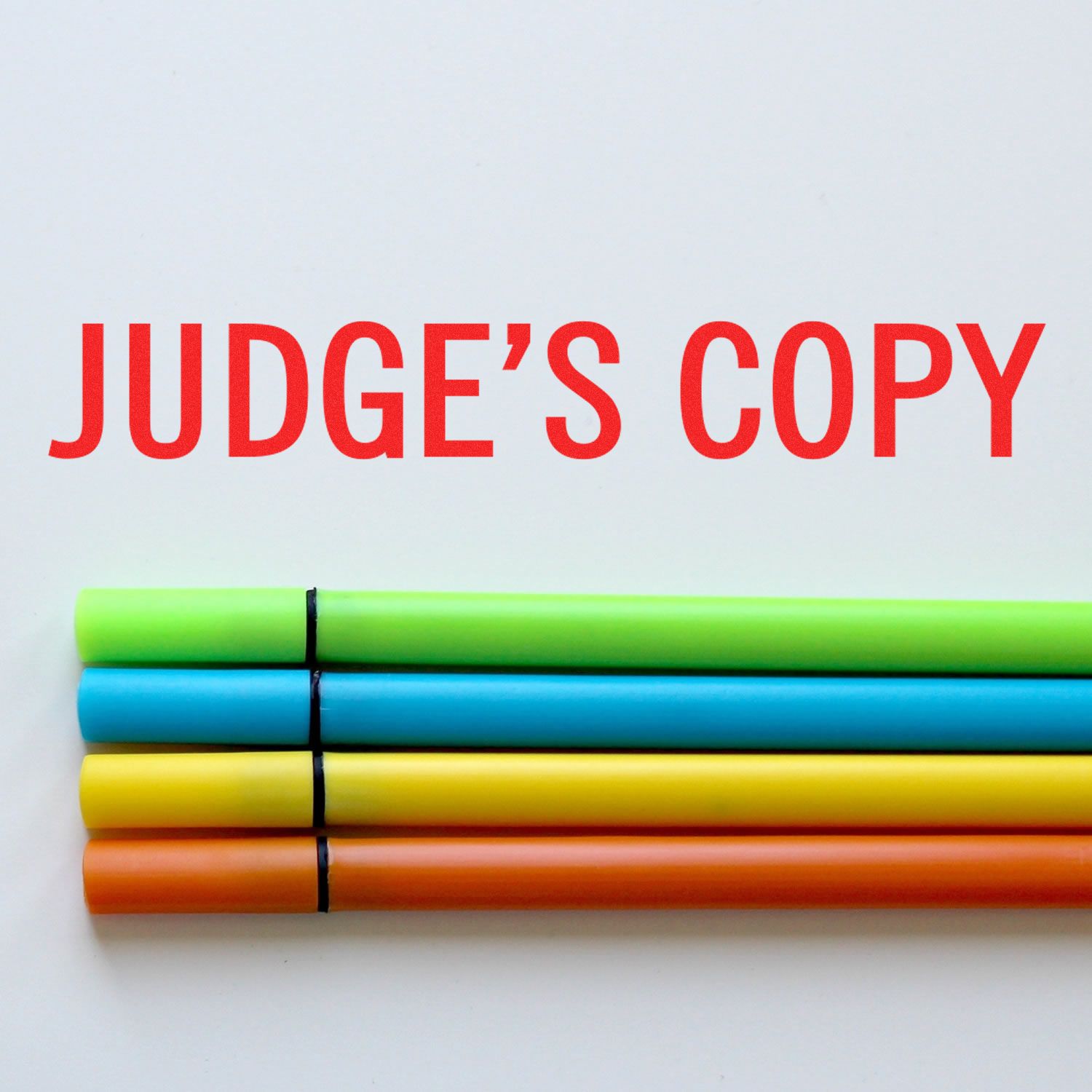 Judge's Copy Rubber Stamp in red ink on white paper, with four colorful markers (green, blue, yellow, orange) aligned below the text.