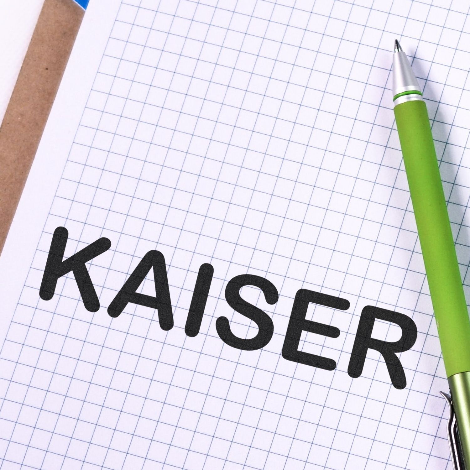 A green pen rests on graph paper stamped with the word "KAISER" using the Medical Kaiser Rubber Stamp.