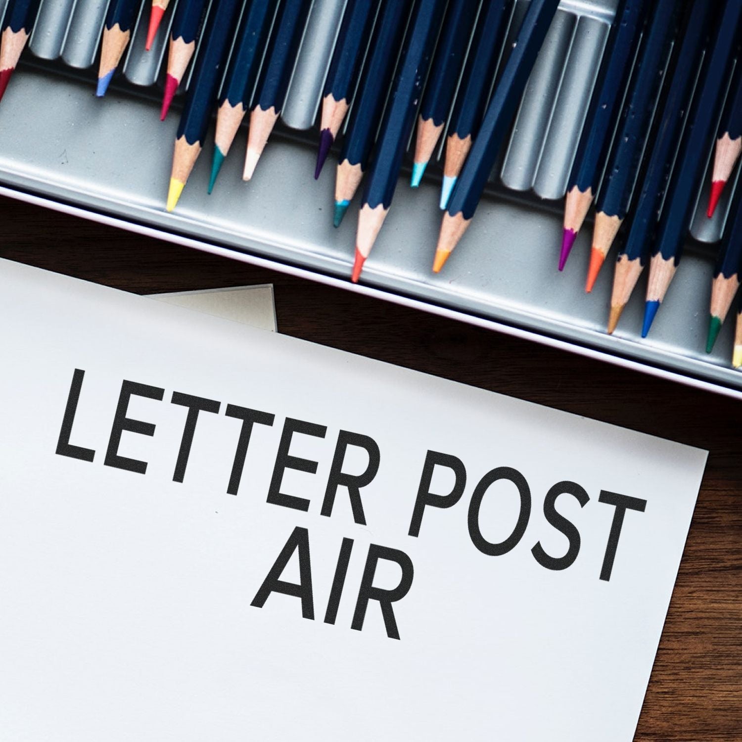 Self Inking Letter Post Air Stamp used on a white envelope, with colored pencils in the background.