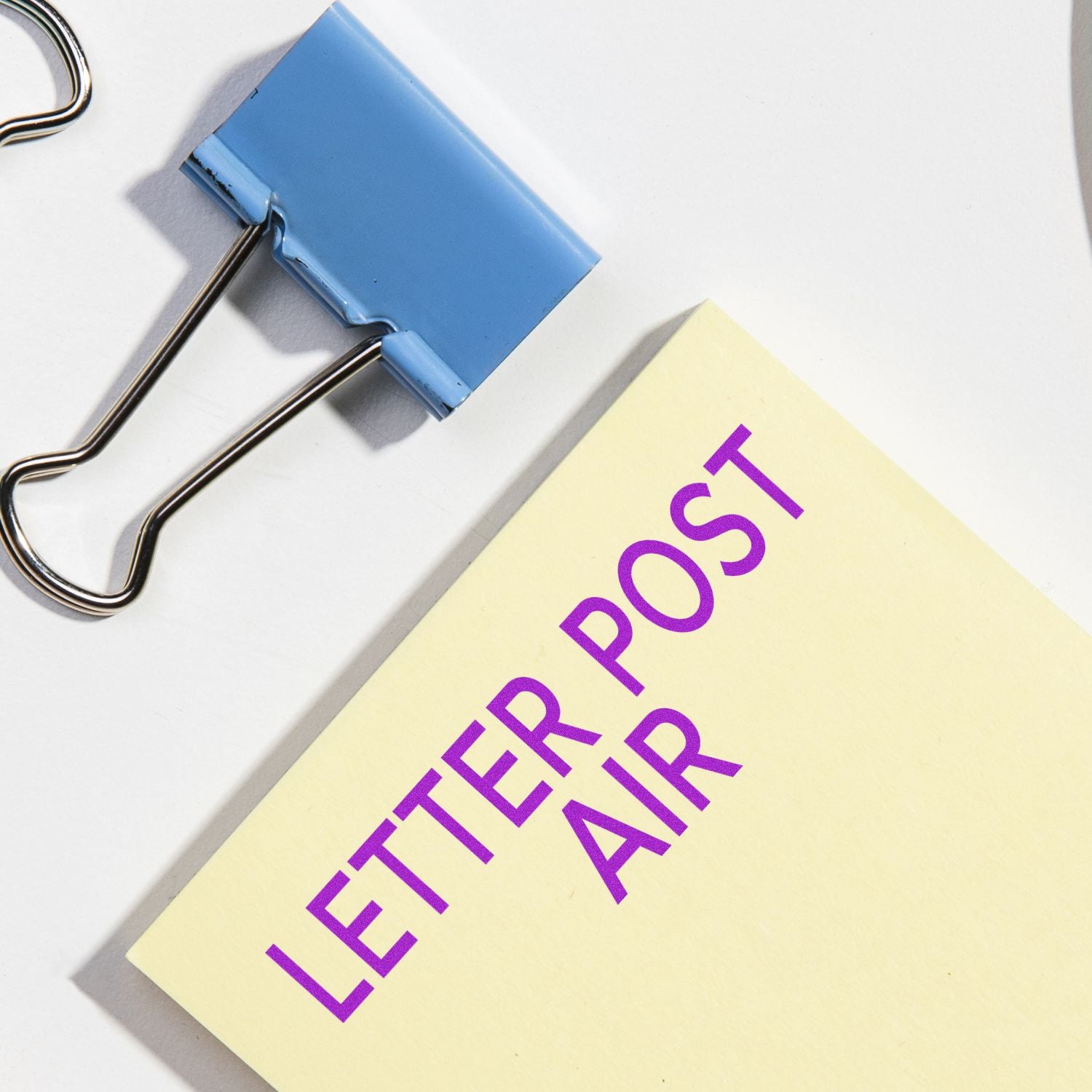 Large Self Inking Letter Post Air Stamp imprint on a yellow paper next to a blue binder clip on a white surface.