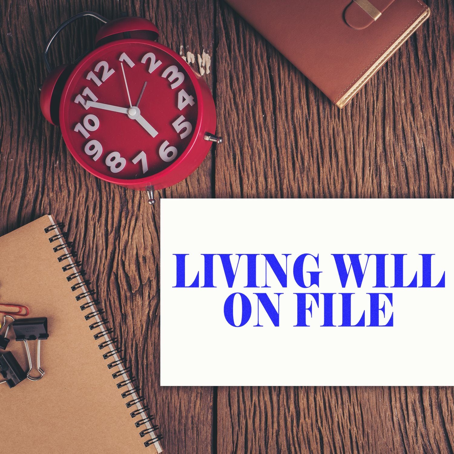 Large Self Inking Living Will On File Stamp used on a white paper, placed on a wooden desk with a red clock, notebook, and binder clips.