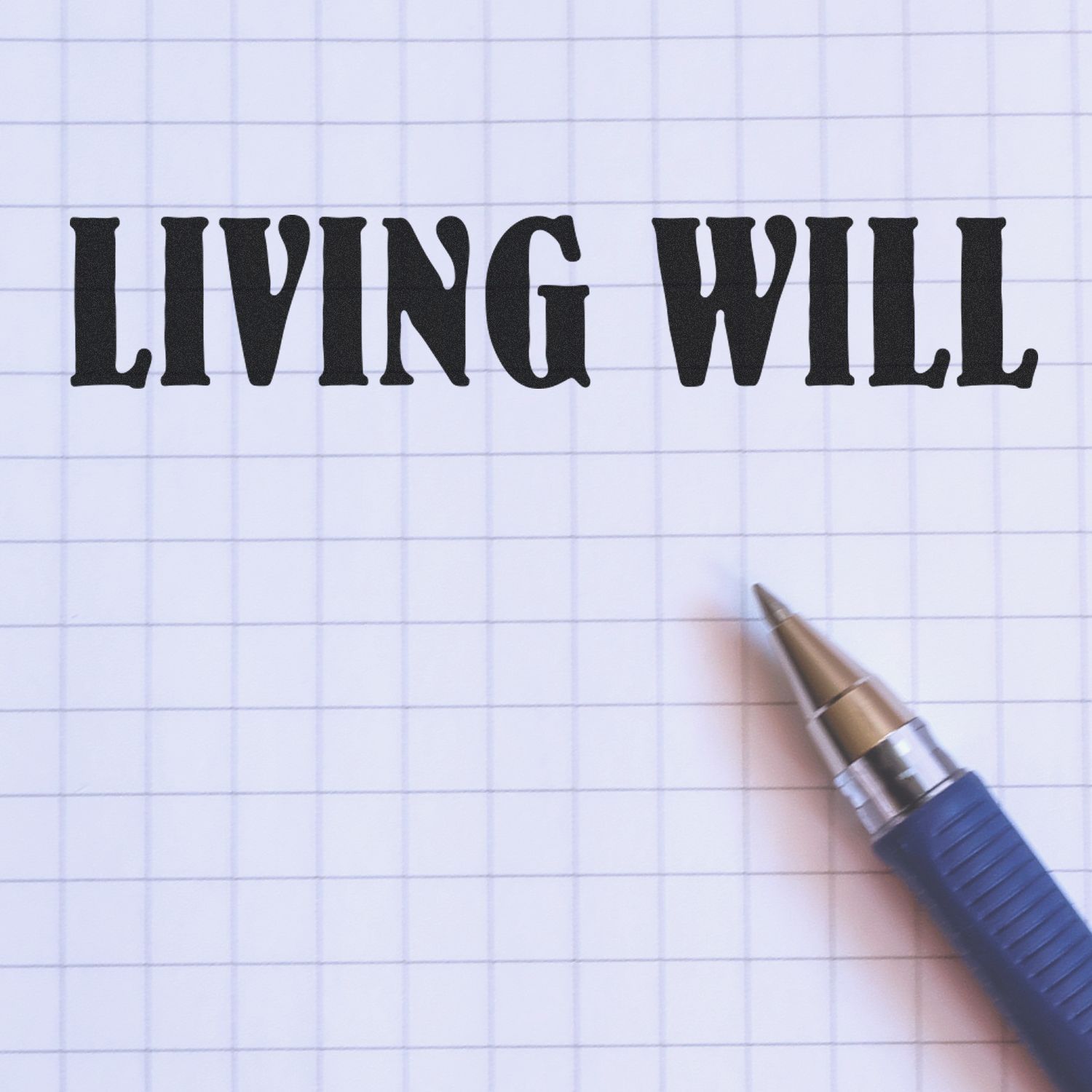 Large Pre-Inked Living Will Stamp used on grid paper with a blue pen beside it, displaying the text 'LIVING WILL' in bold black letters.