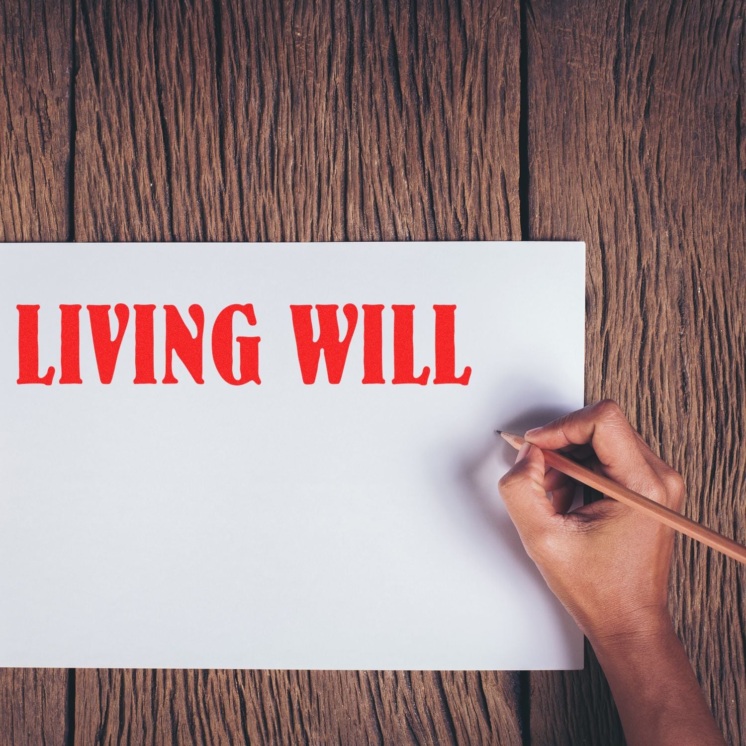 Hand holding a pencil next to a paper stamped with LIVING WILL in red using the Large Self Inking Living Will Stamp on a wooden surface.