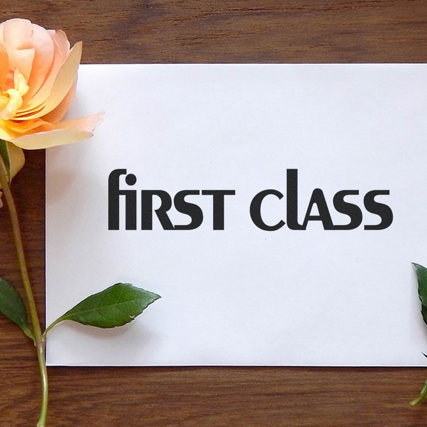 Envelope stamped with 'first class' using a Slim Pre-Inked Lower Case First Class Stamp, placed on a wooden table with a rose.