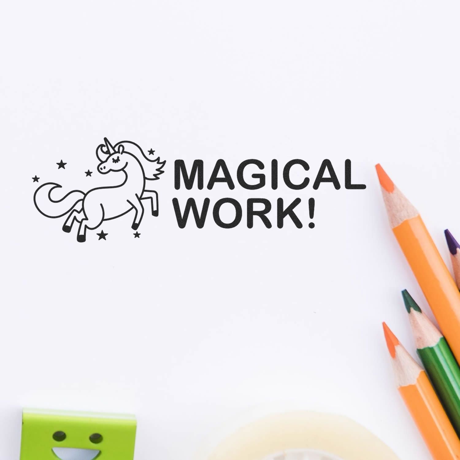 Large Self Inking Magical Work Stamp imprint with a unicorn and stars, surrounded by colorful pencils and a tape dispenser on a white surface.