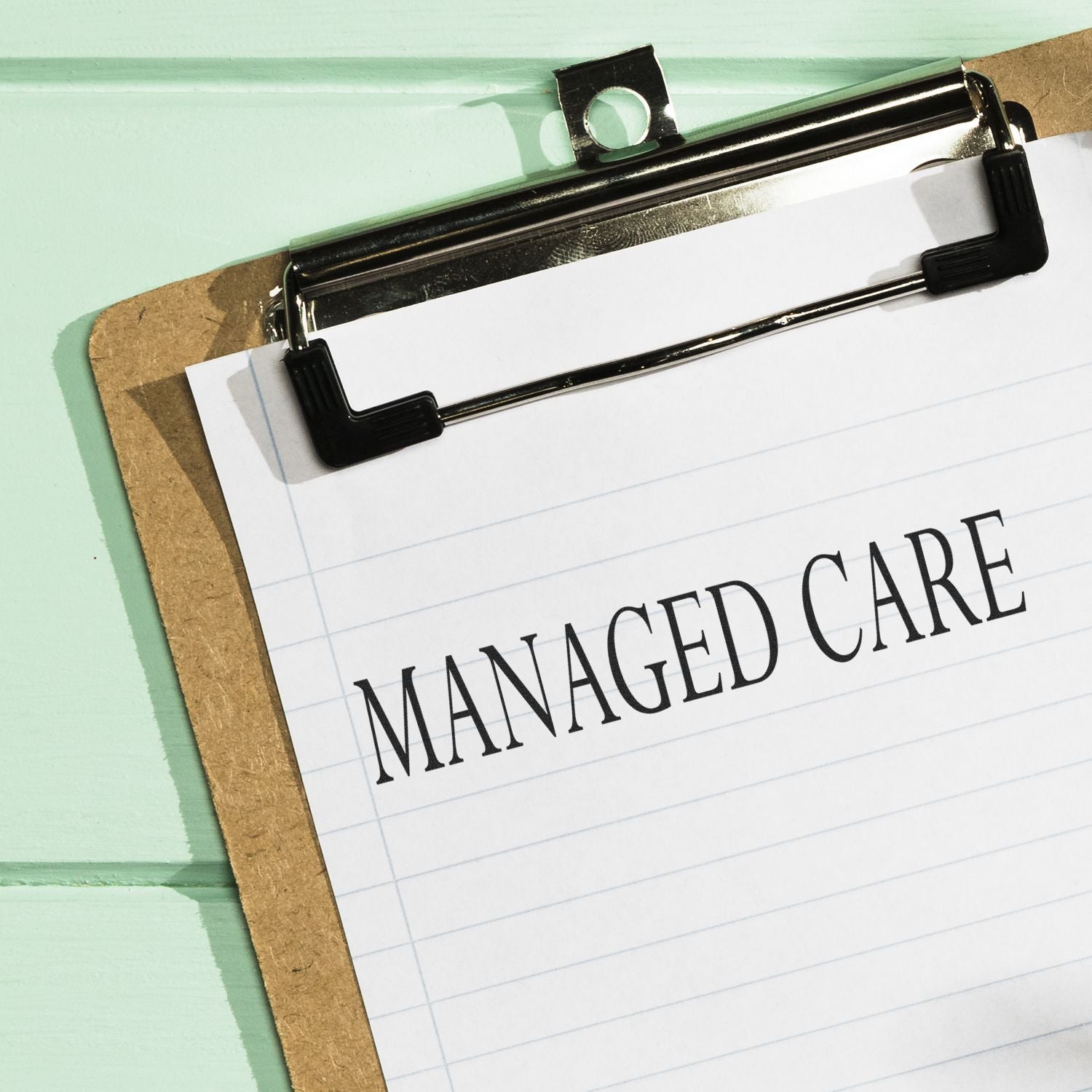 Clipboard with a sheet of paper stamped Managed Care using a Slim Pre-Inked Managed Care Stamp, placed on a light green surface.