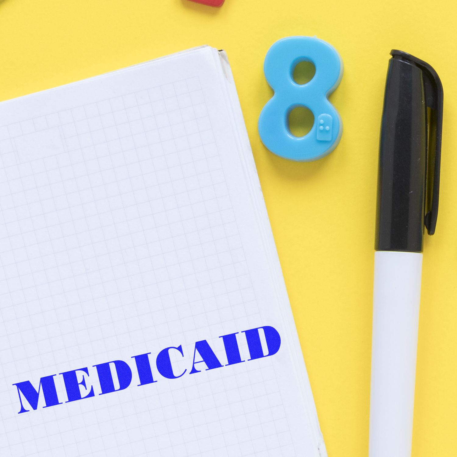 Large Self Inking Medicaid Stamp in use on a notebook with a pen and a blue number 8 on a yellow background.