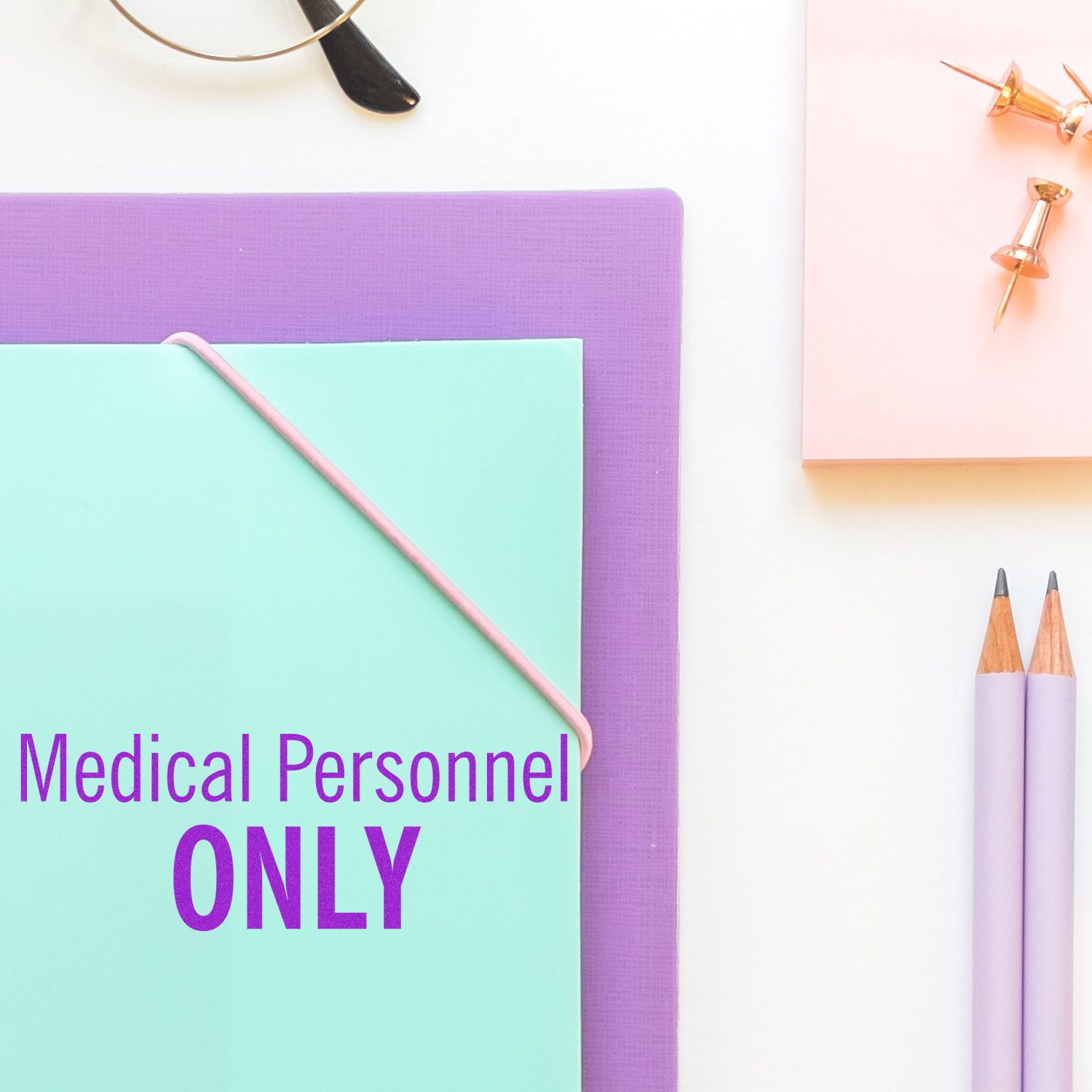 Large Pre-Inked Medical Personnel Only Stamp used on a mint green folder, surrounded by office supplies like pencils, push pins, and glasses.