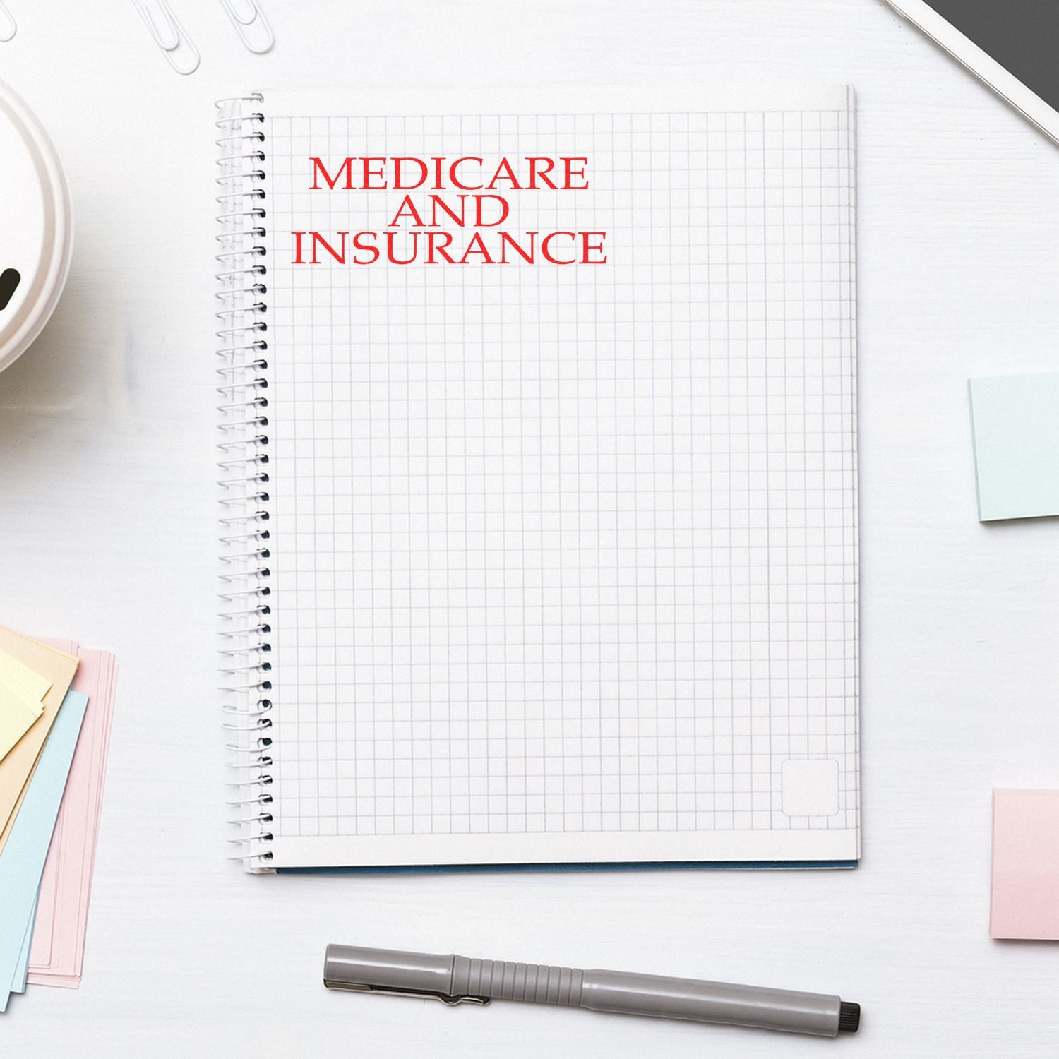 Large Self Inking Medicare And Insurance Stamp in red ink on a spiral notebook, surrounded by office supplies on a white desk.