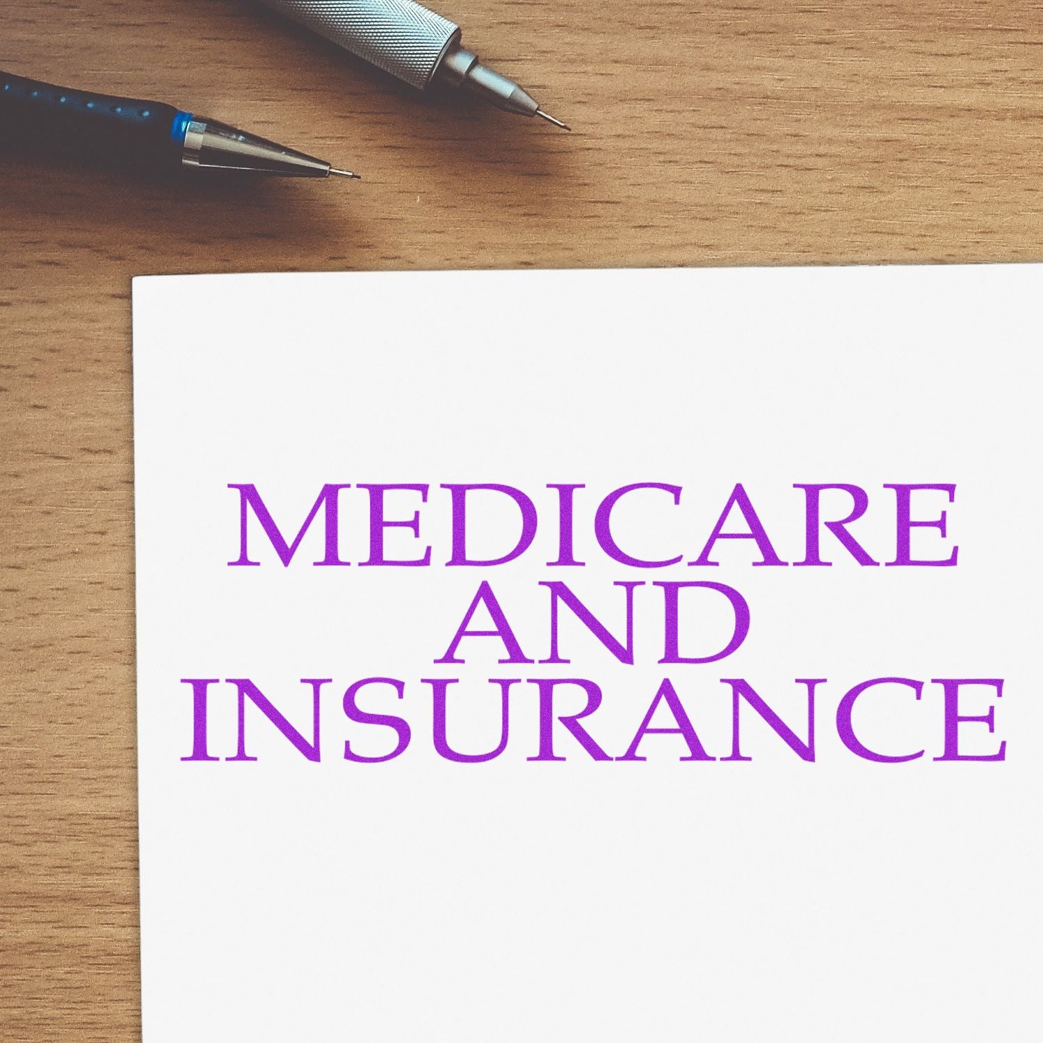 Large Medicare And Insurance Rubber Stamp in purple ink on white paper, placed on a wooden desk with two pens in the background.