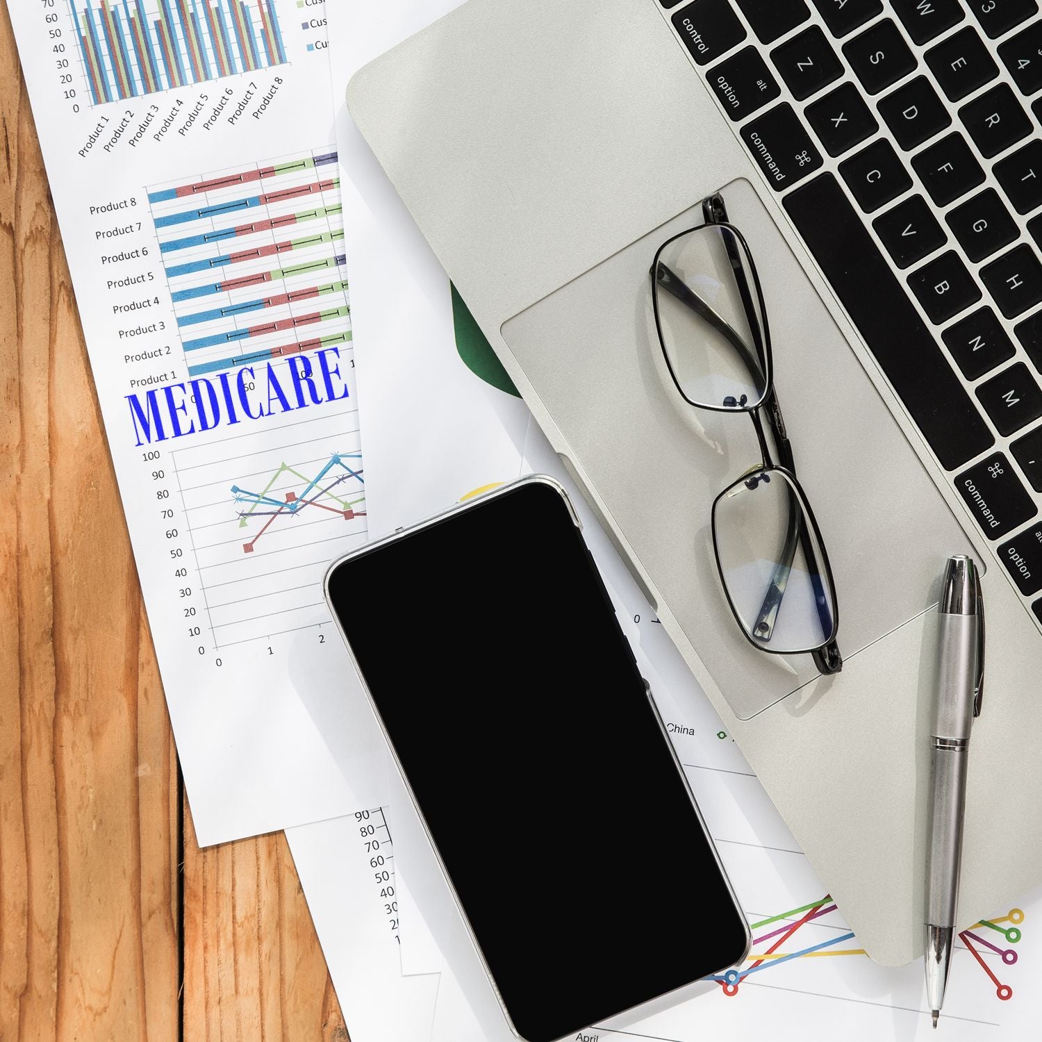 Large Self Inking Medicare Stamp on a document beside a laptop, glasses, smartphone, and pen on a wooden desk.