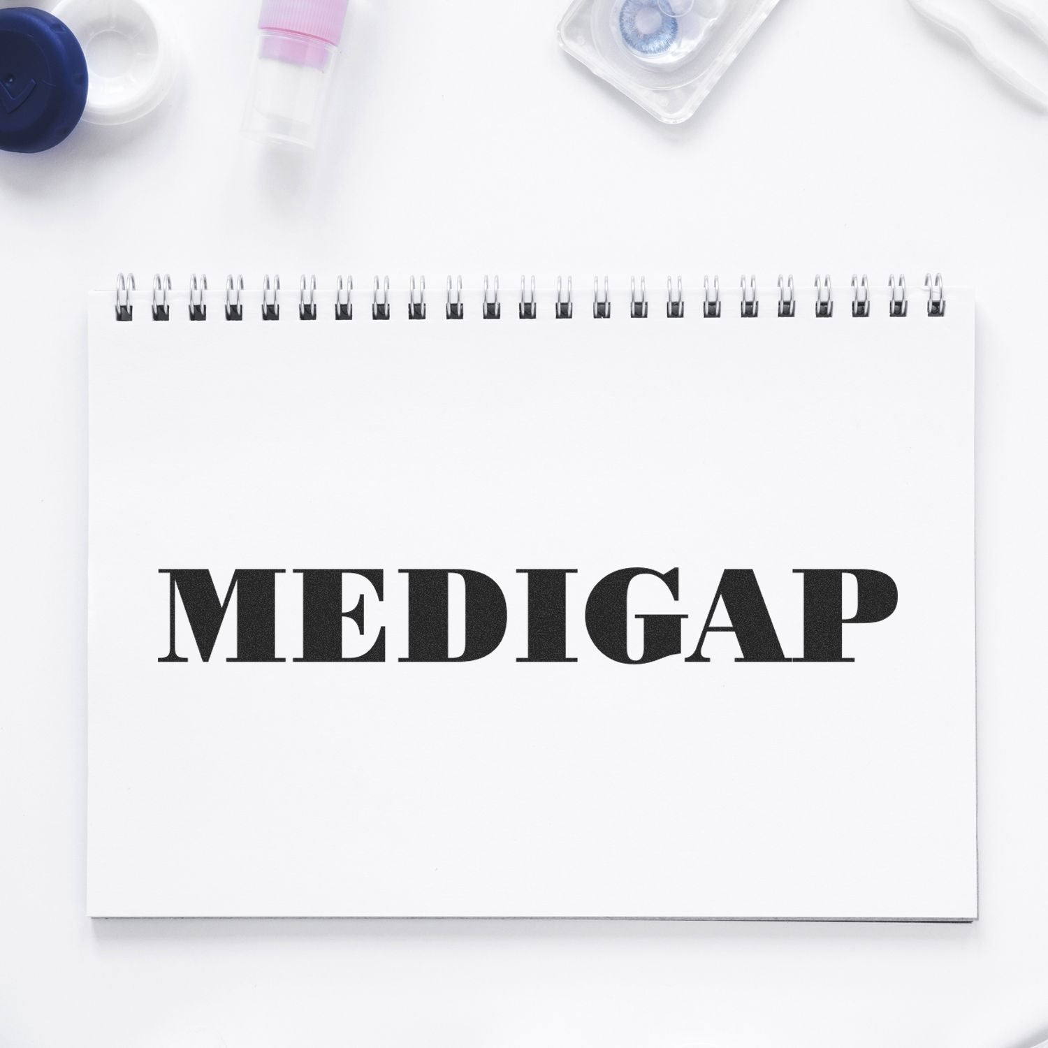 A Large Self Inking Medigap Stamp imprint on a white spiral notebook, surrounded by medical supplies on a white background.