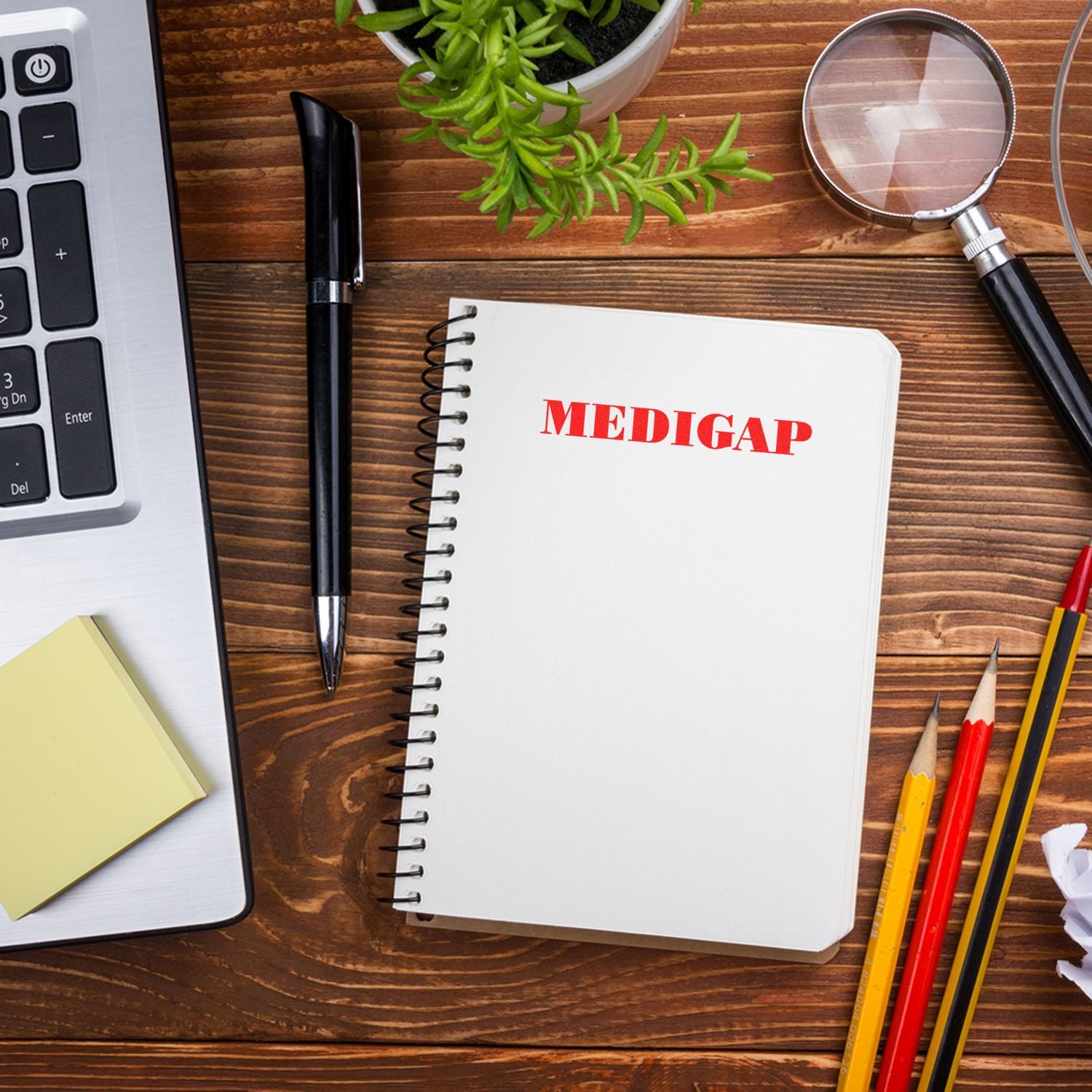 Slim Pre-Inked Medigap Stamp used on a notebook, placed on a wooden desk with a laptop, pen, plant, magnifying glass, and pencils.