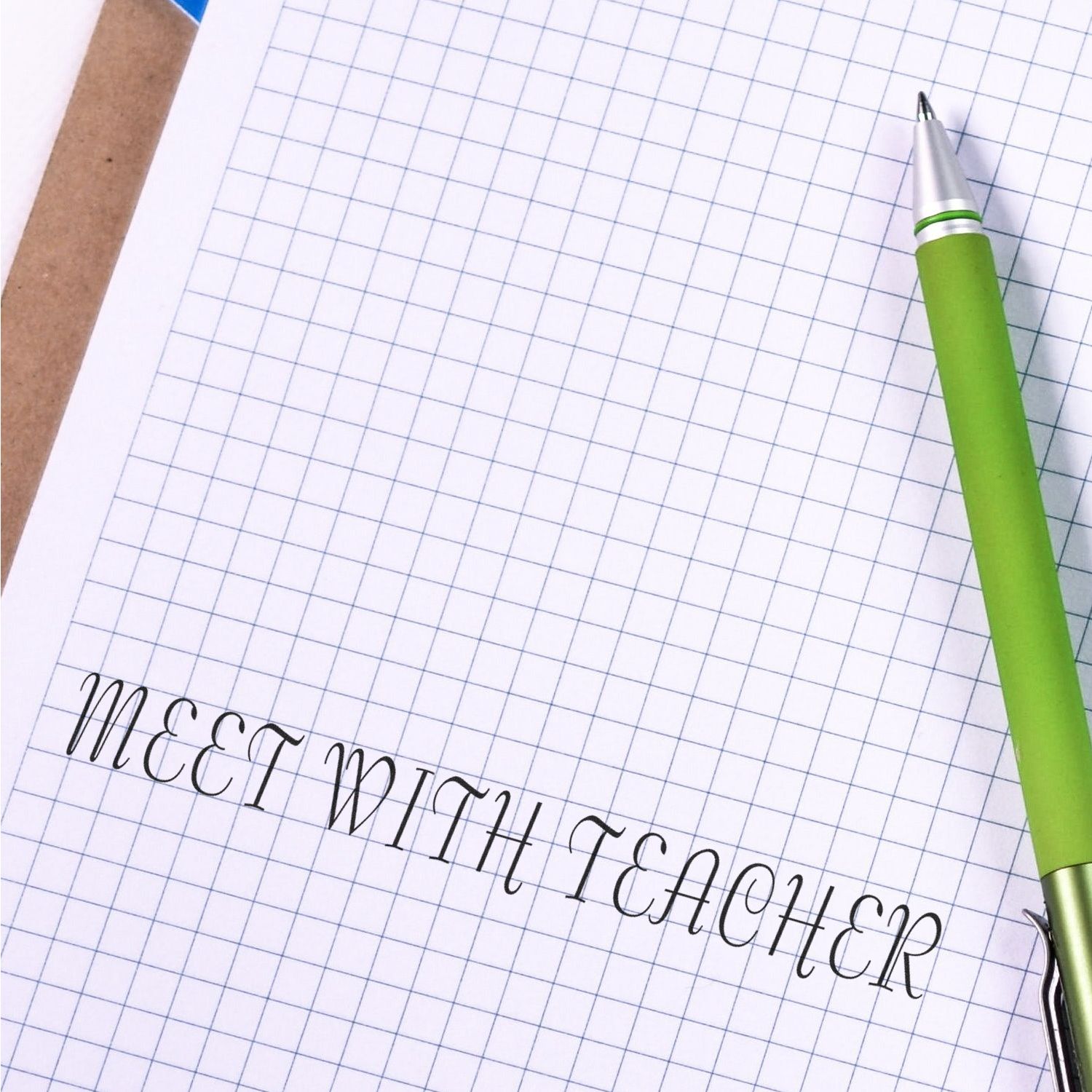 Large Self Inking Meet With Teacher Stamp on graph paper with a green pen beside it.