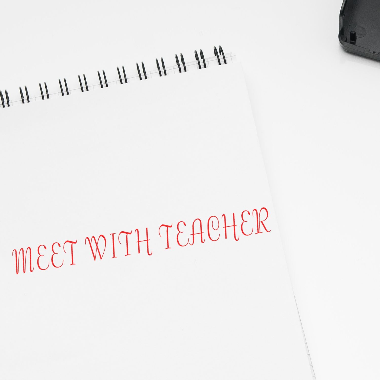 Large Self Inking Meet With Teacher Stamp in red ink on a white spiral notebook, with the stamp pad partially visible in the corner.