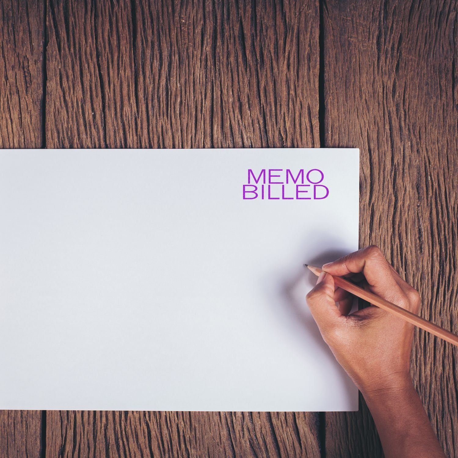 Hand holding pencil next to a stamped MEMO BILLED on white paper, using the Large Memo Billed Rubber Stamp, on a wooden surface.