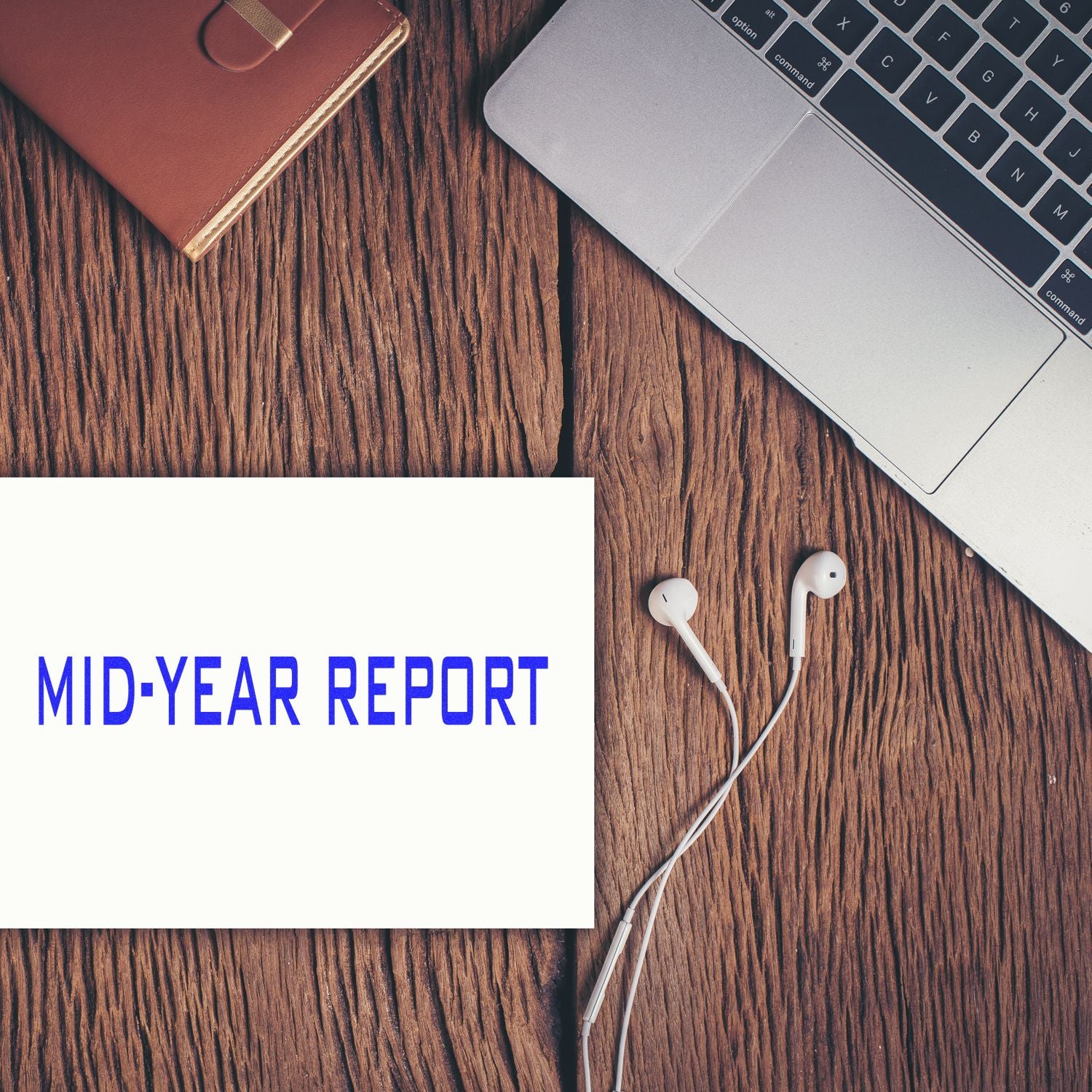 Slim Pre-Inked Mid Year Report Stamp on a white paper beside a laptop, notebook, and earphones on a wooden desk.