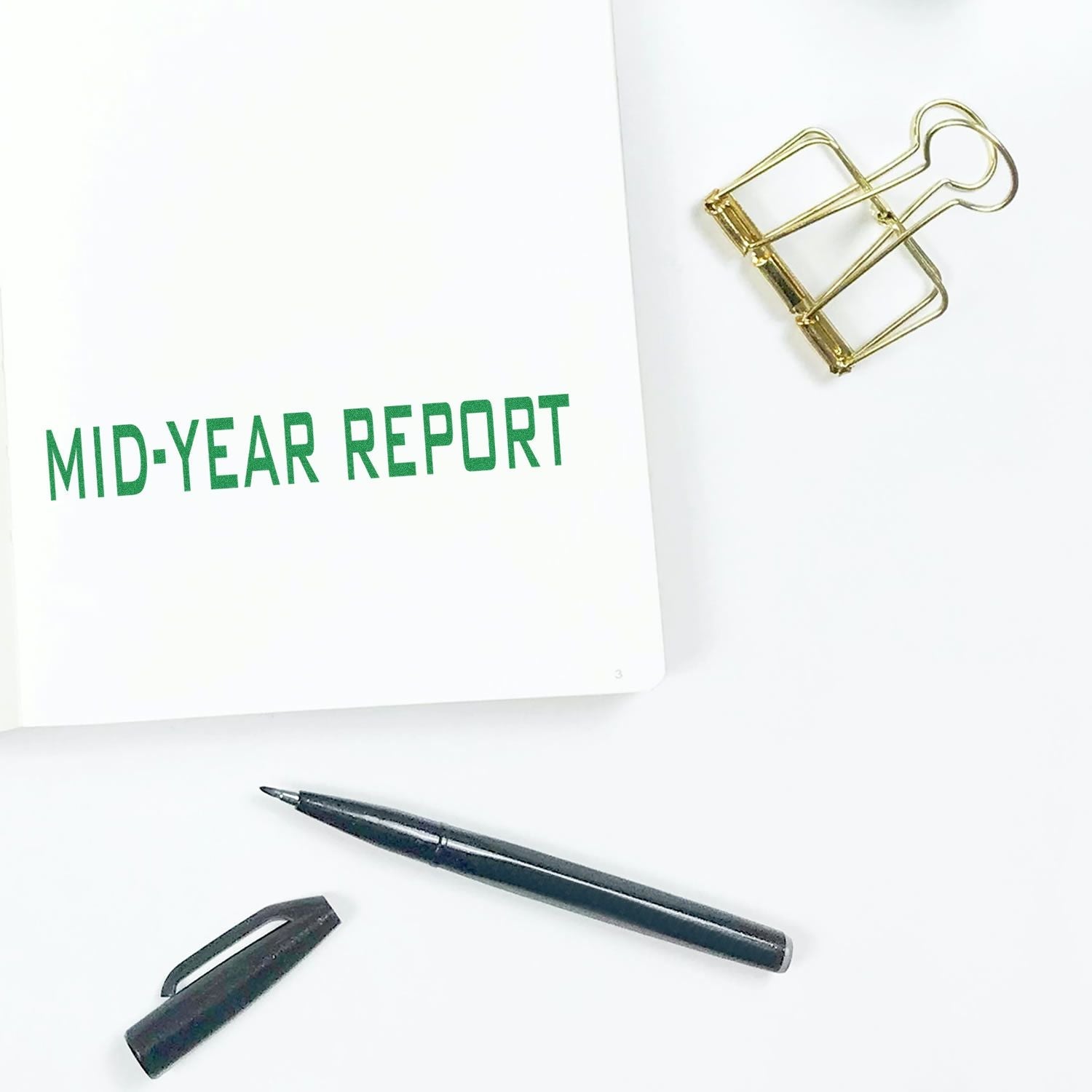 Self Inking Mid Year Report Stamp used on a white paper, with a black pen, pen cap, and a gold binder clip nearby.