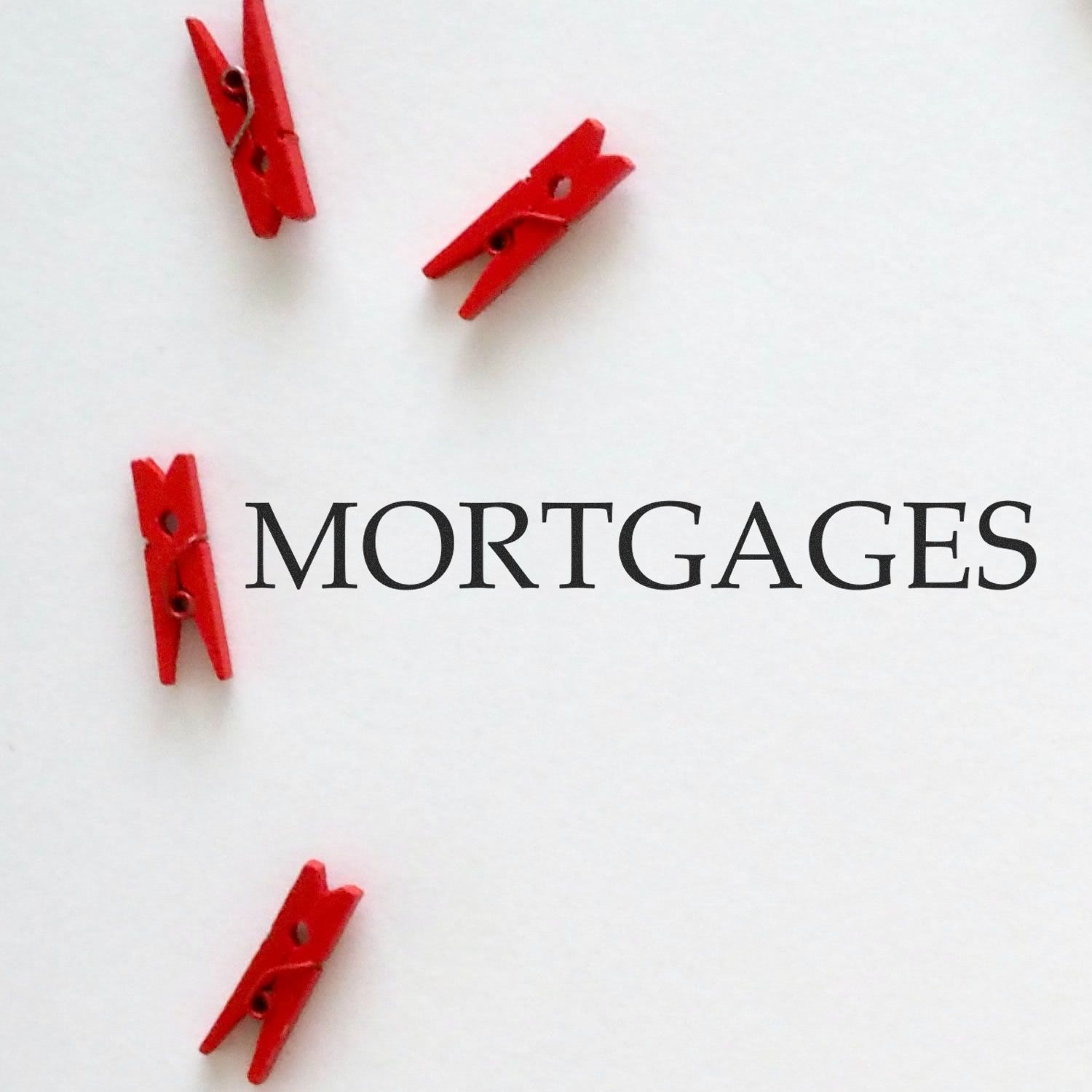 Large Pre-Inked Mortgages Stamp in use, stamping the word MORTGAGES on white paper with red clothespins scattered around.