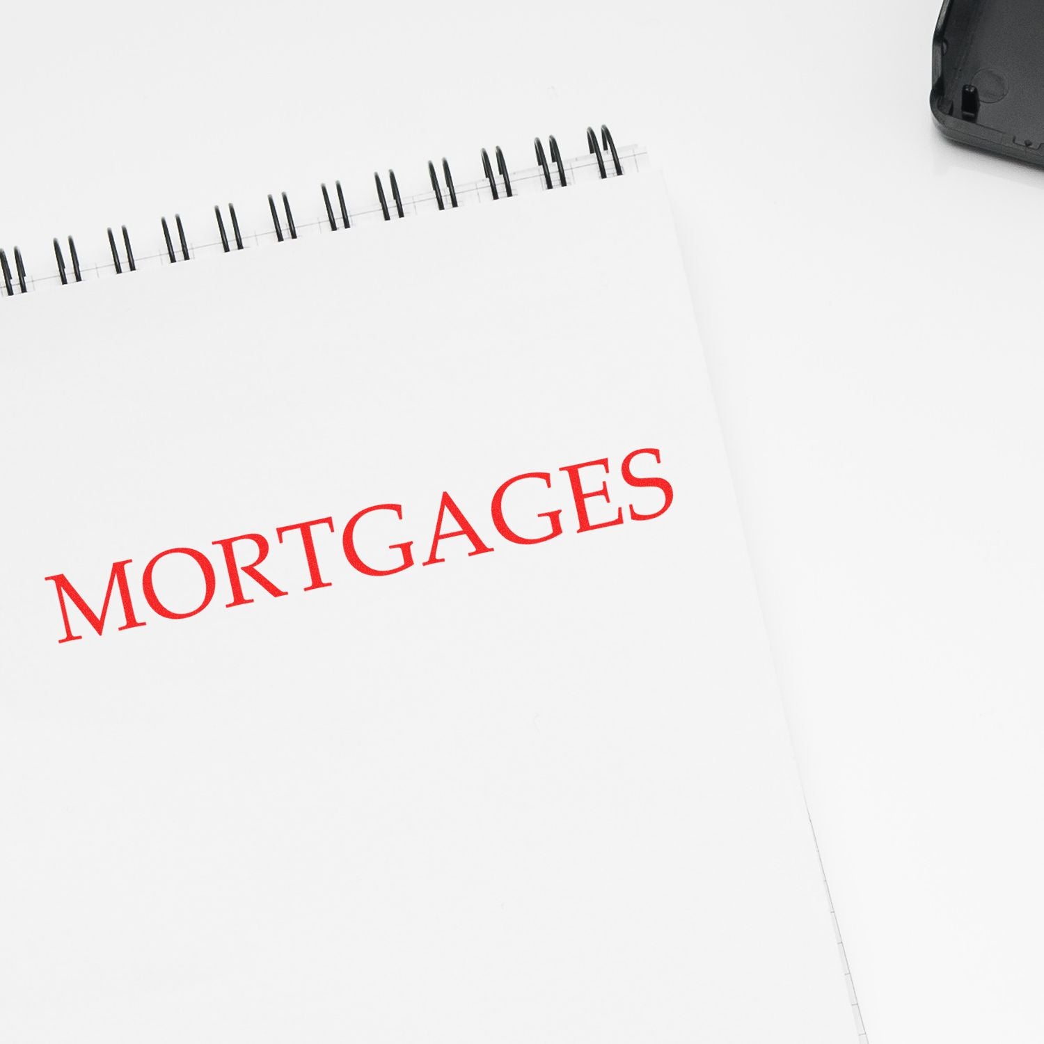 Large Pre-Inked Mortgages Stamp in use, stamping the word MORTGAGES in red ink on a white spiral-bound notebook.