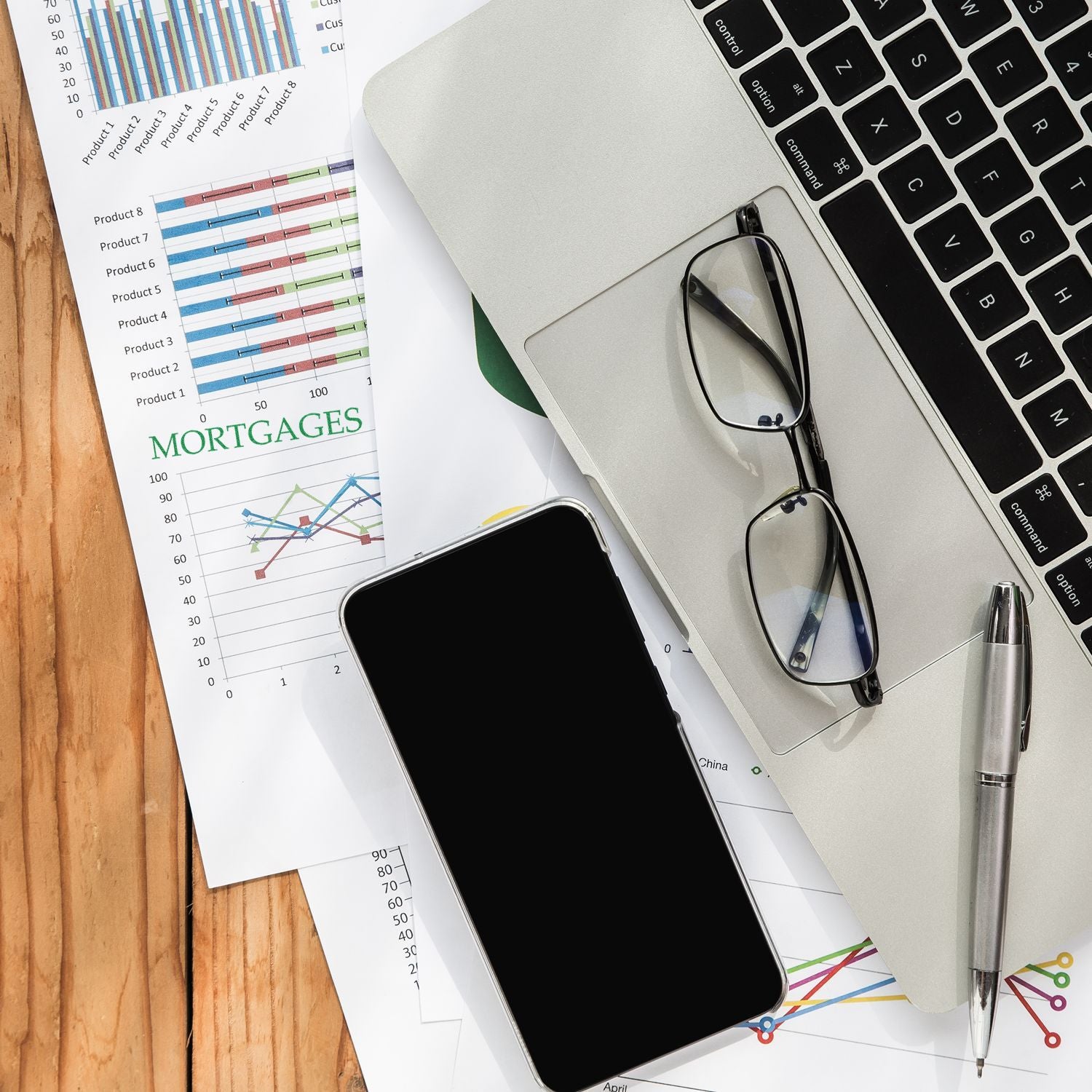 A desk with a Large Self Inking Mortgages Stamp, laptop, glasses, smartphone, pen, and mortgage charts.