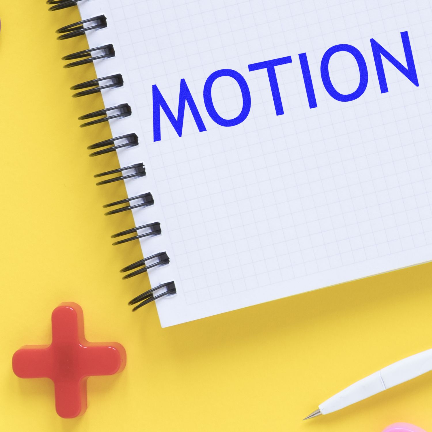 Large Self Inking Motion Stamp in use, stamping the word MOTION in blue on a white notepad, with a yellow background and red cross-shaped object.