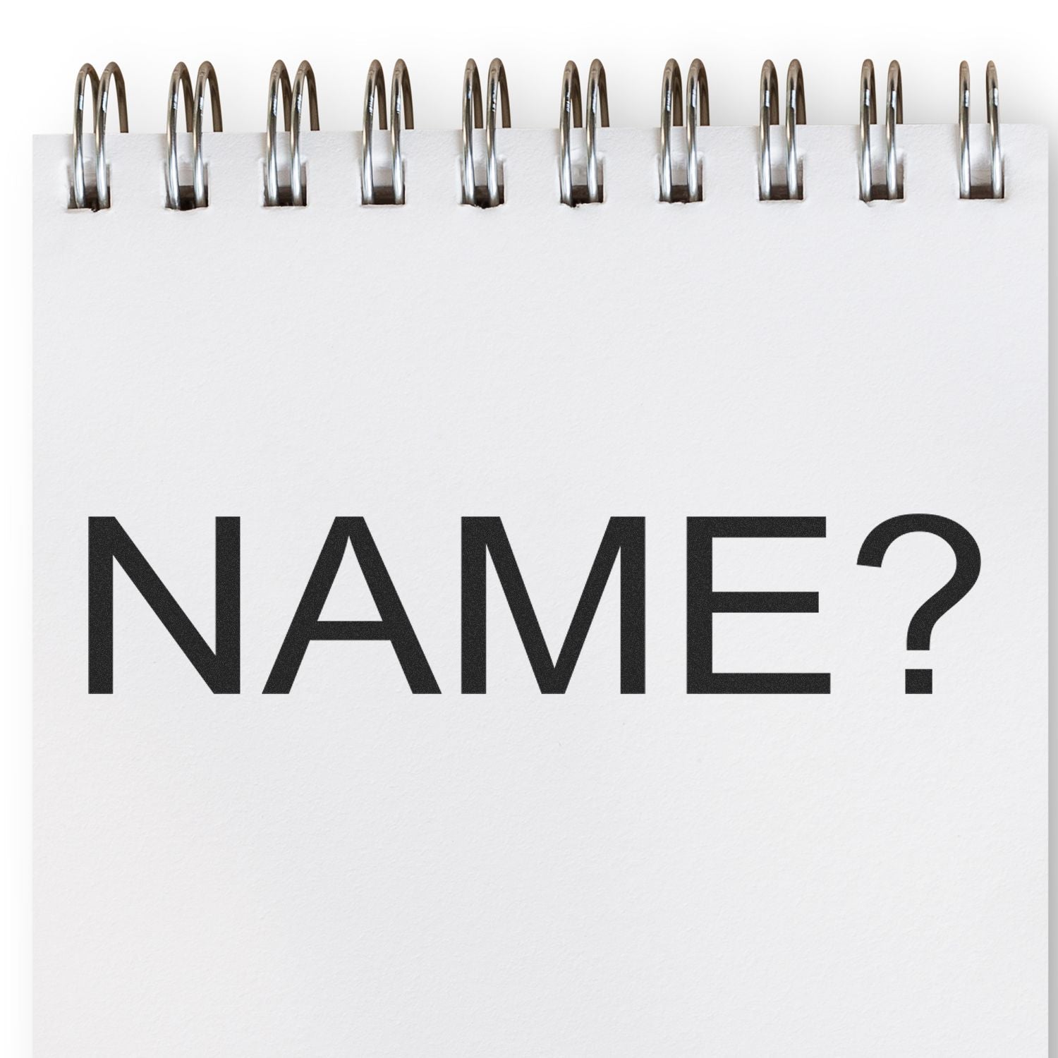 A Large Pre-Inked Name Stamp is shown in use on a spiral-bound notepad with the word NAME? stamped in bold black letters.